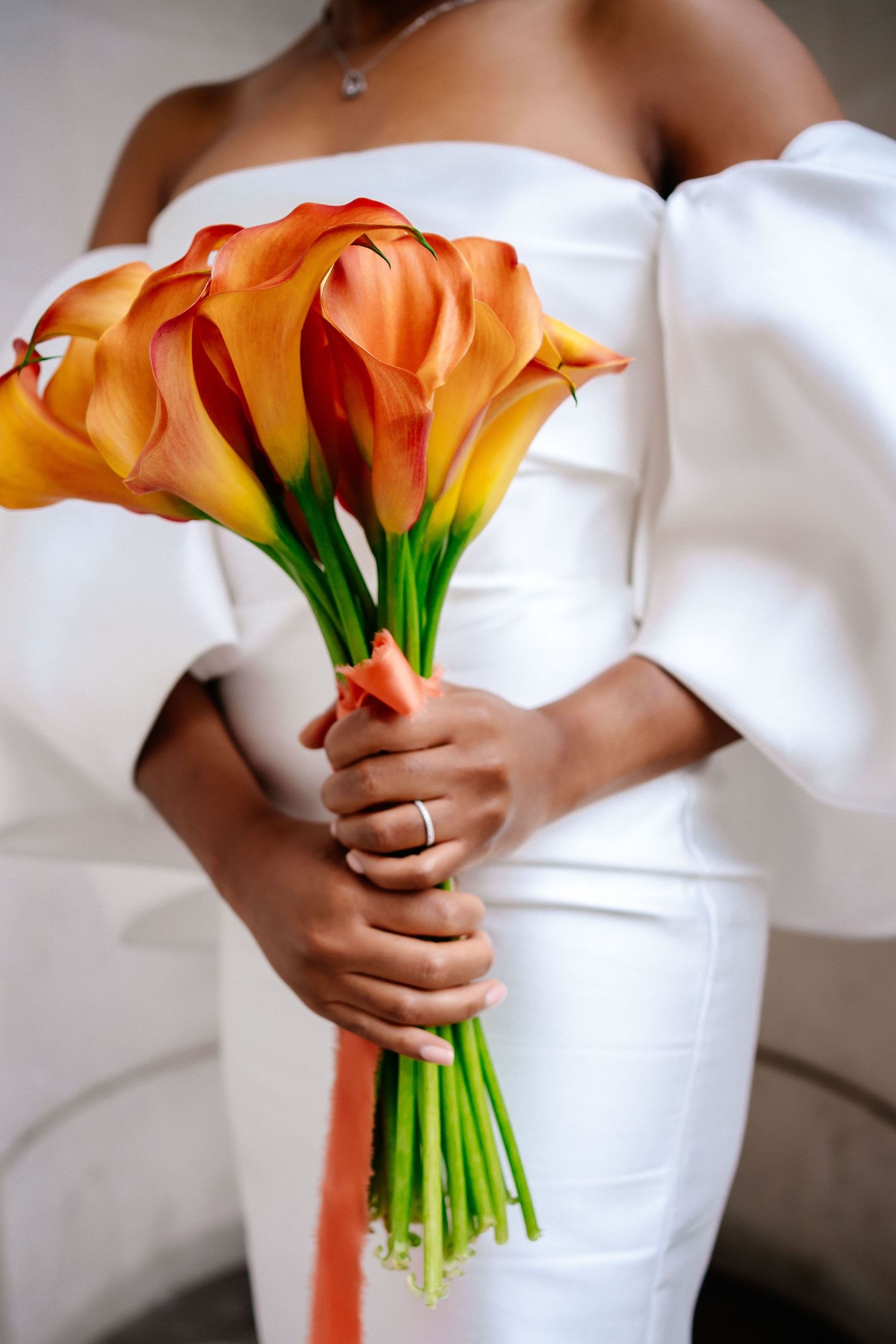 Elegant bridal bouquet of orange calla lilies against white wedding dress.