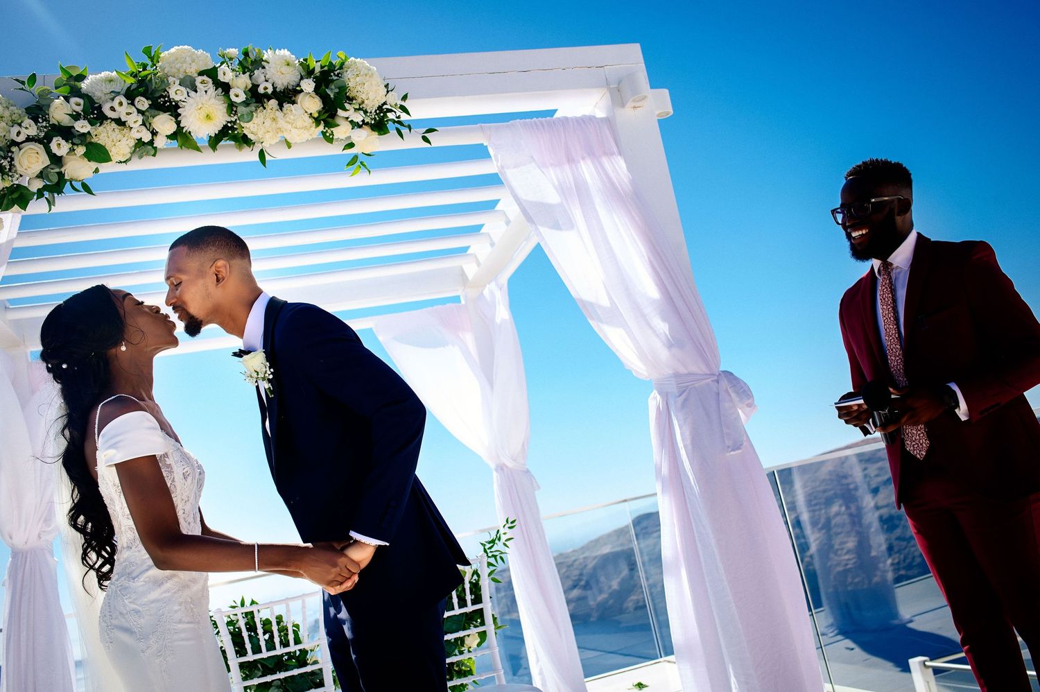 Wedding ceremony setup with white draped columns against bright blue sky.