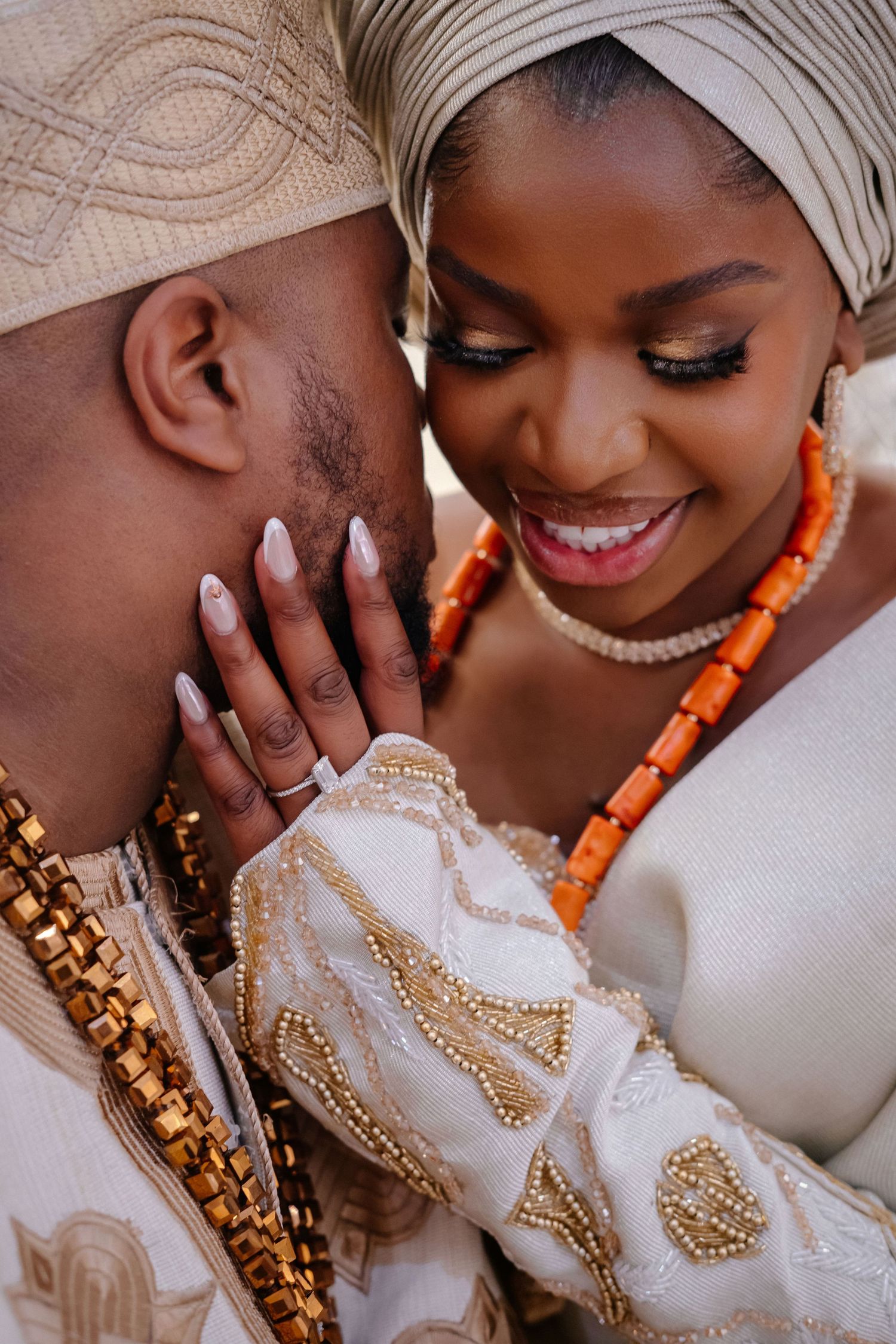 Close-up portrait of a couple in traditional West African wedding attire with white and gold fabrics and coral beaded jewelry.