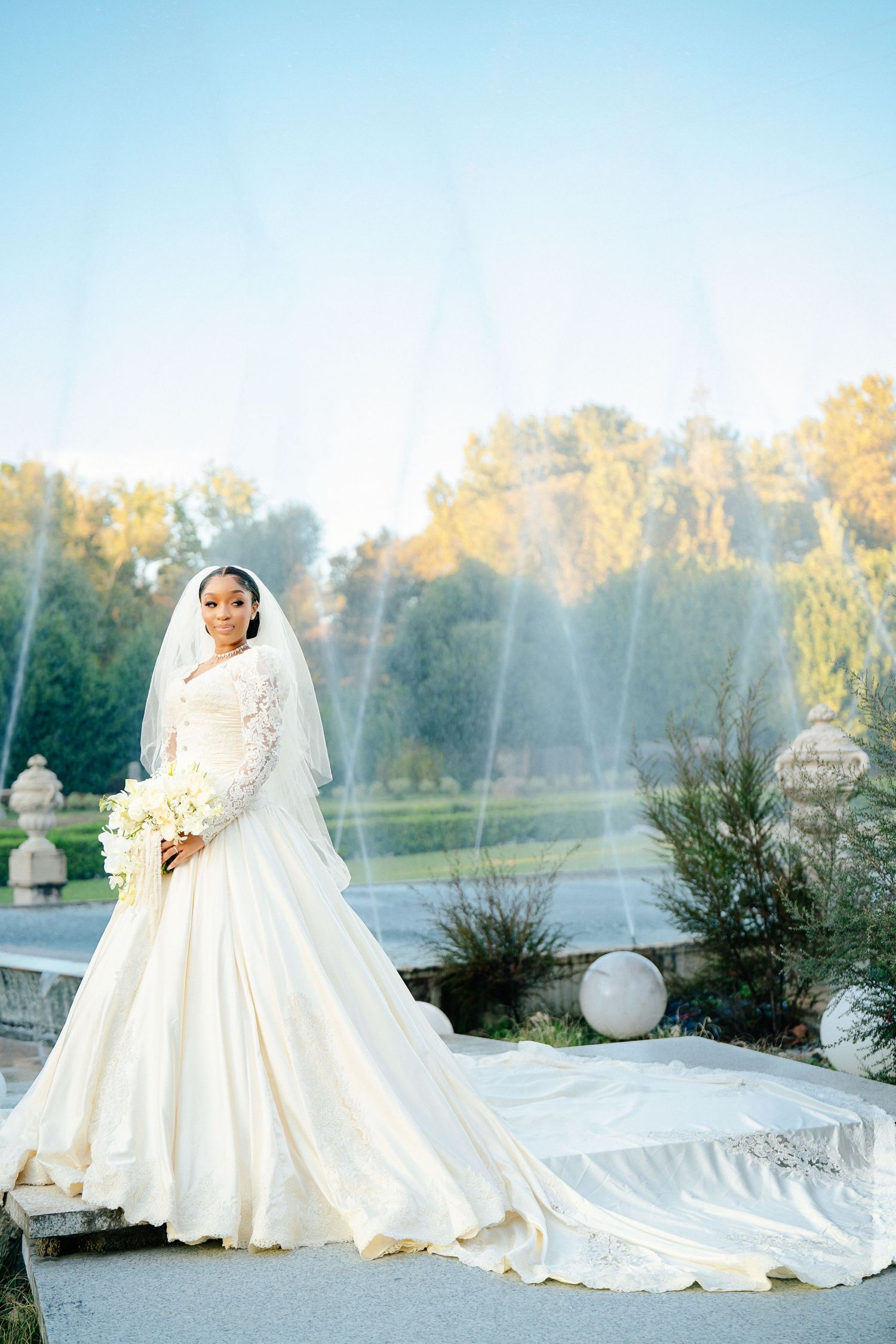 Stunning bridal portraits in flowing white gown with cathedral veil against natural backdrop.