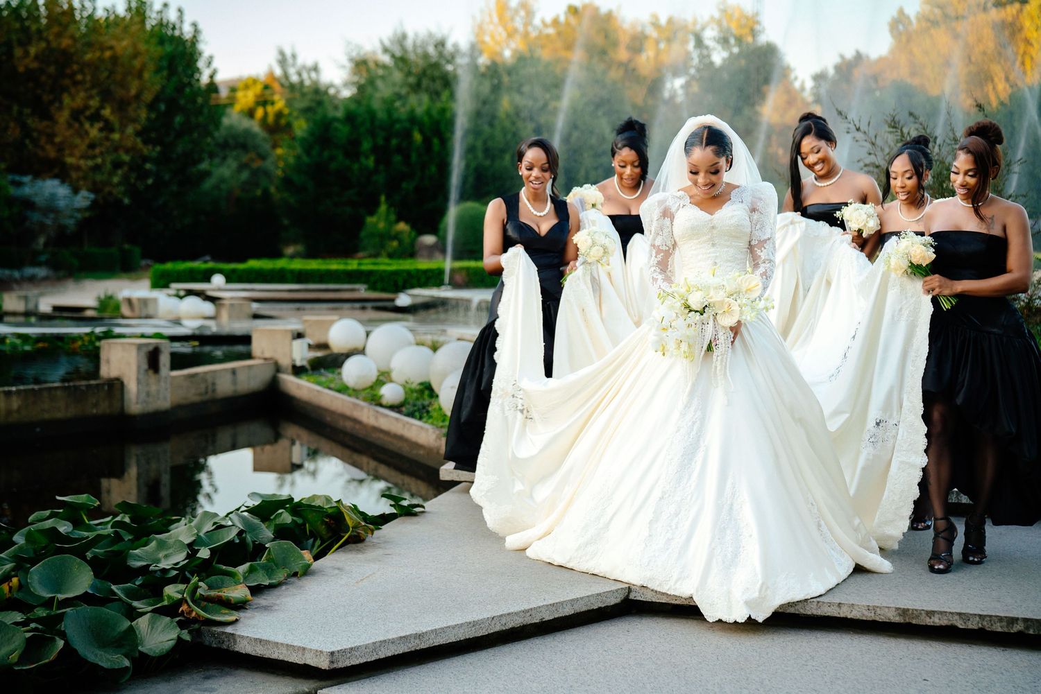 Wedding party poses outdoors in elegant attire on stone steps during sunset.