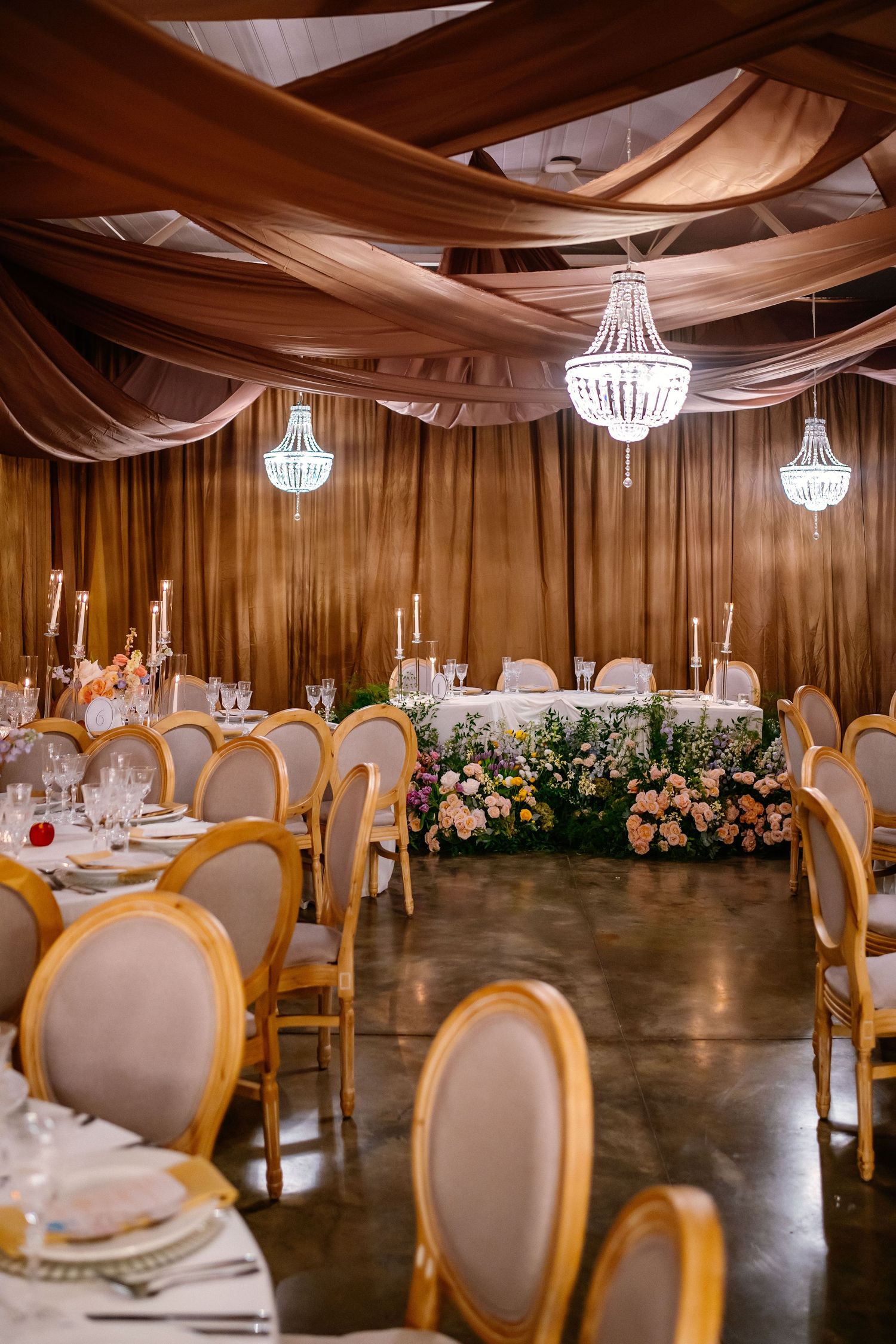Elegant wedding reception venue with draped fabric ceiling, chandeliers, and gold-framed chairs.