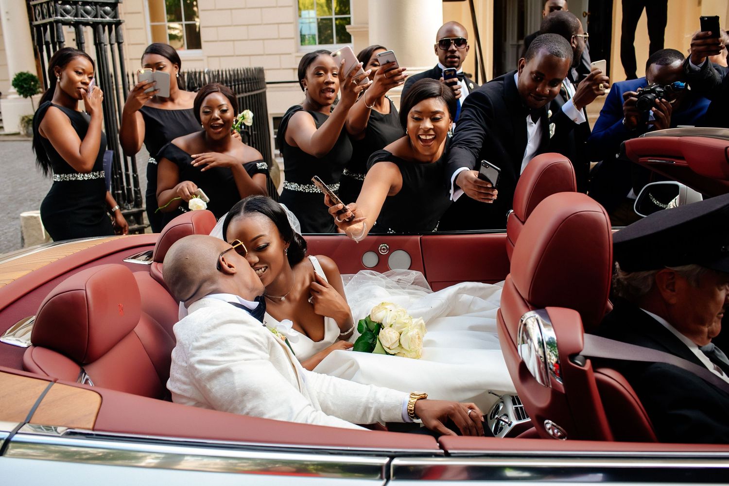 Wedding celebration in classic car with party members cheering and waving.