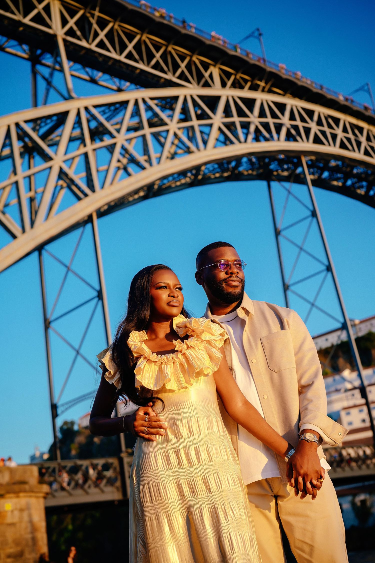 Romantic couple photos under large bridge structure during golden hour.