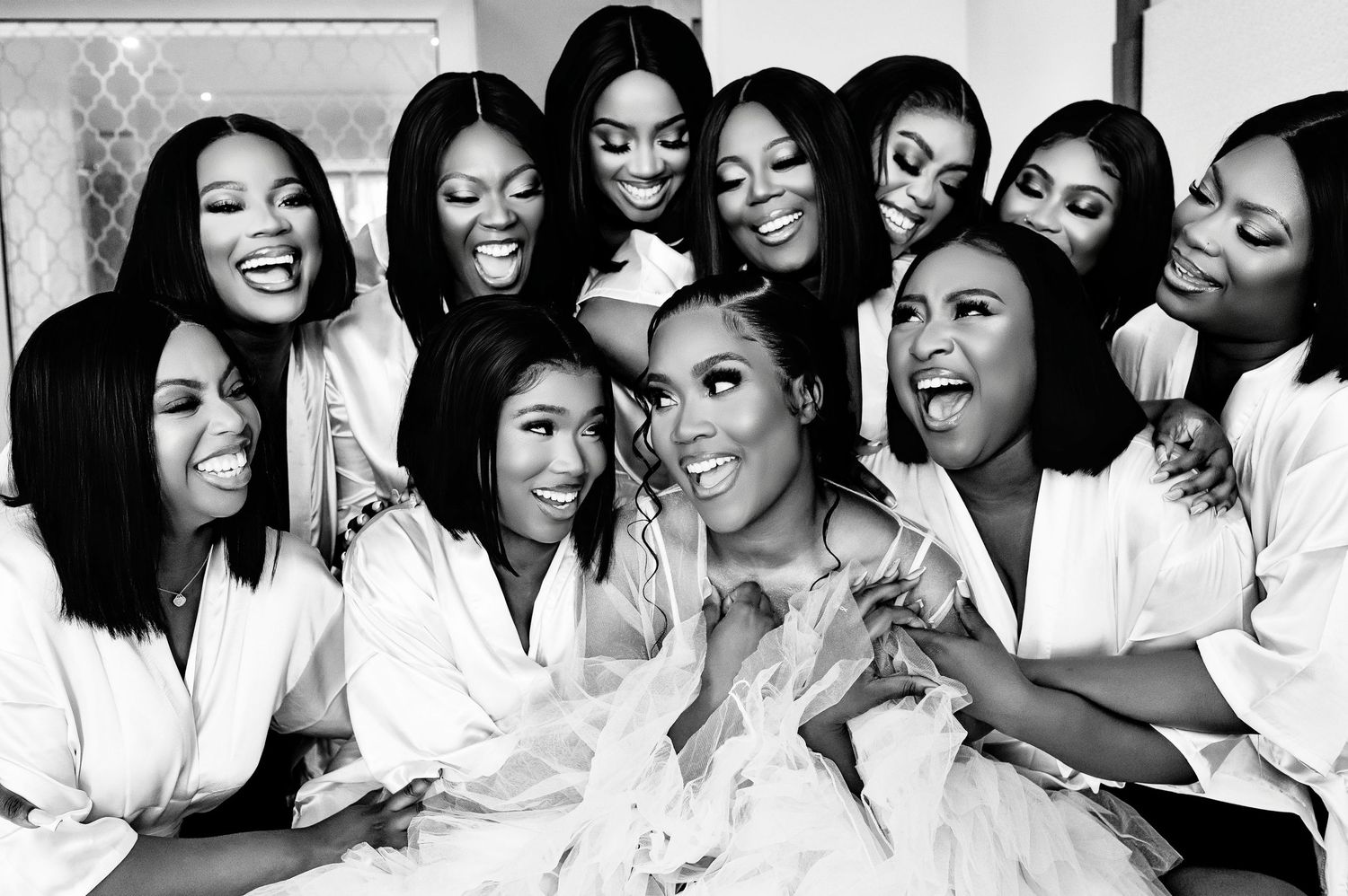 Group of bridesmaids in white robes sharing laughter during wedding preparation.