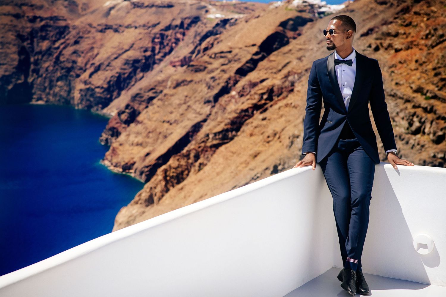 A formal portrait on a white wall overlooking stunning blue waters and rocky cliffs.
