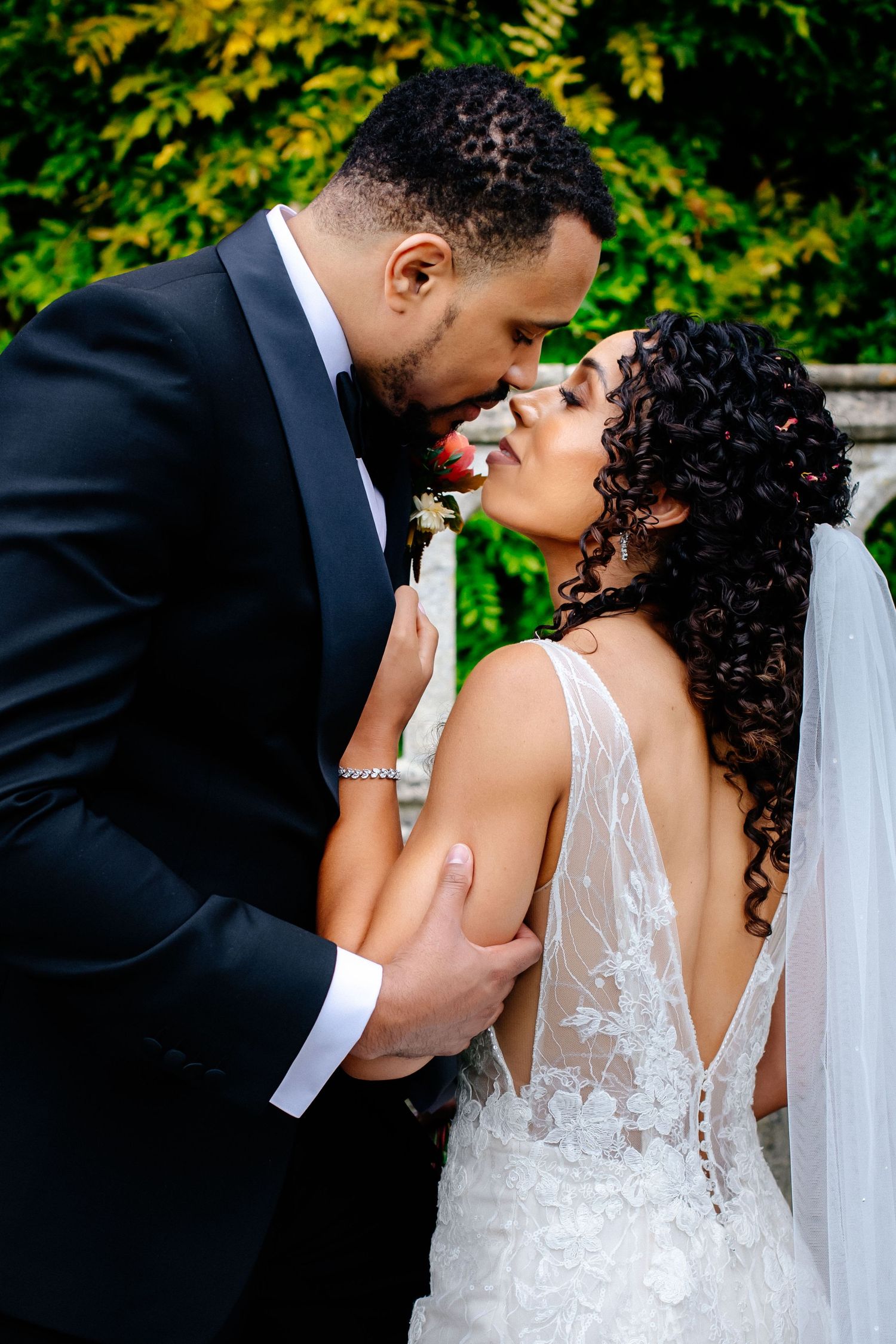 A joyful wedding couple shares a romantic moment outdoors with greenery in the background.
