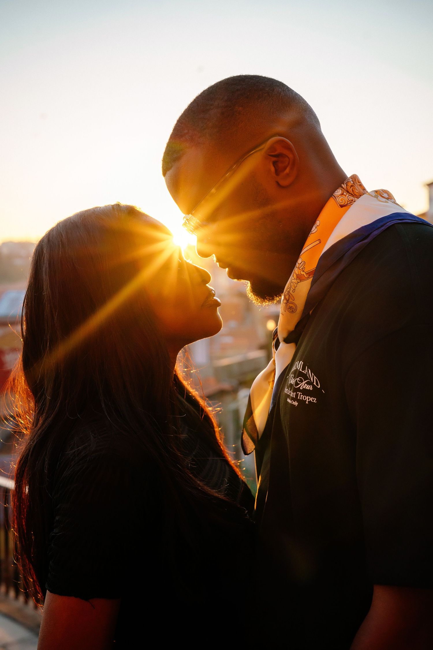 Silhouetted couple sharing an intimate moment at sunset with sun flare creating a warm romantic atmosphere.