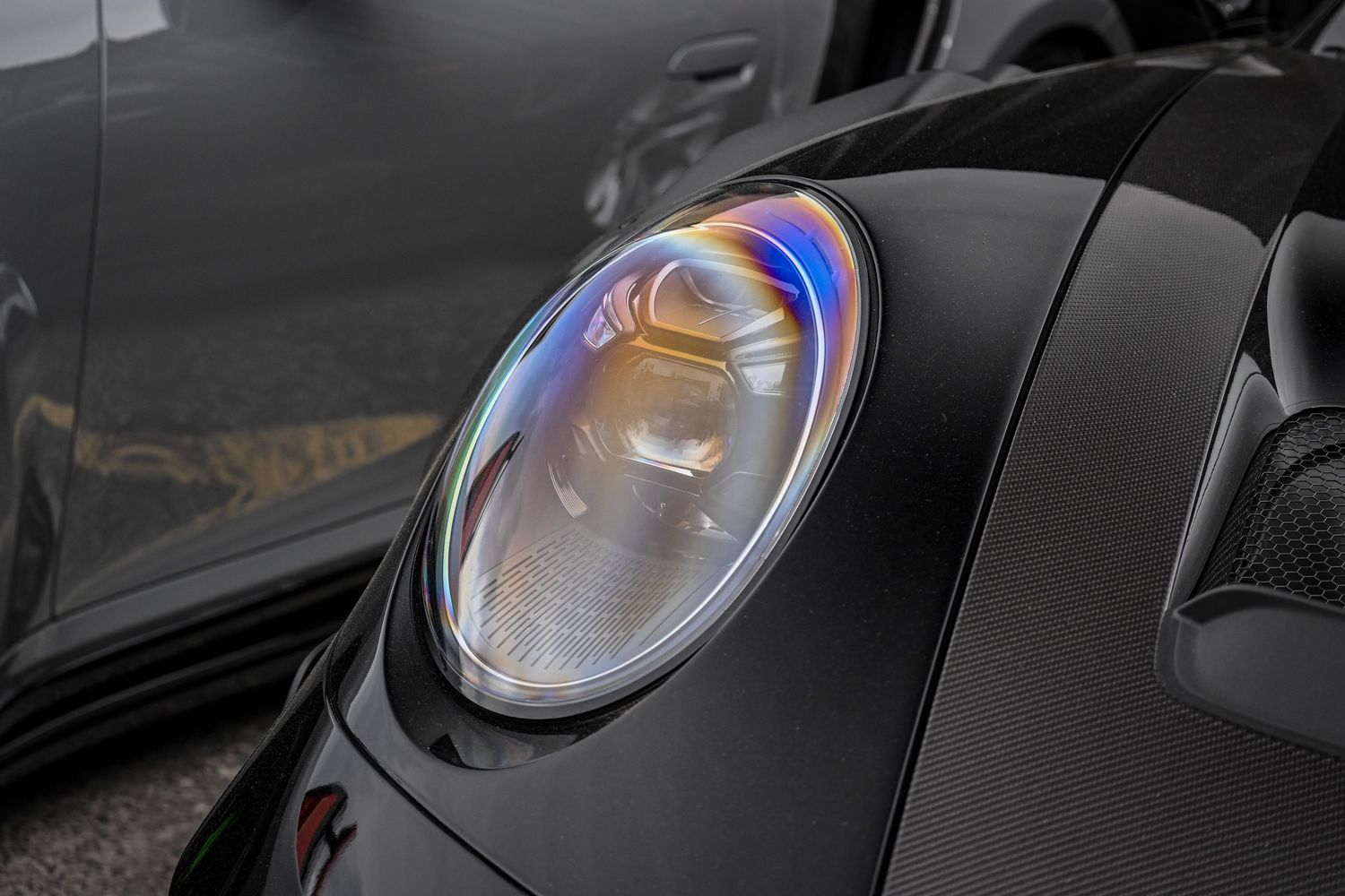 Extreme close-up of a glossy black sports car's circular headlight reflecting bright blue and orange light.