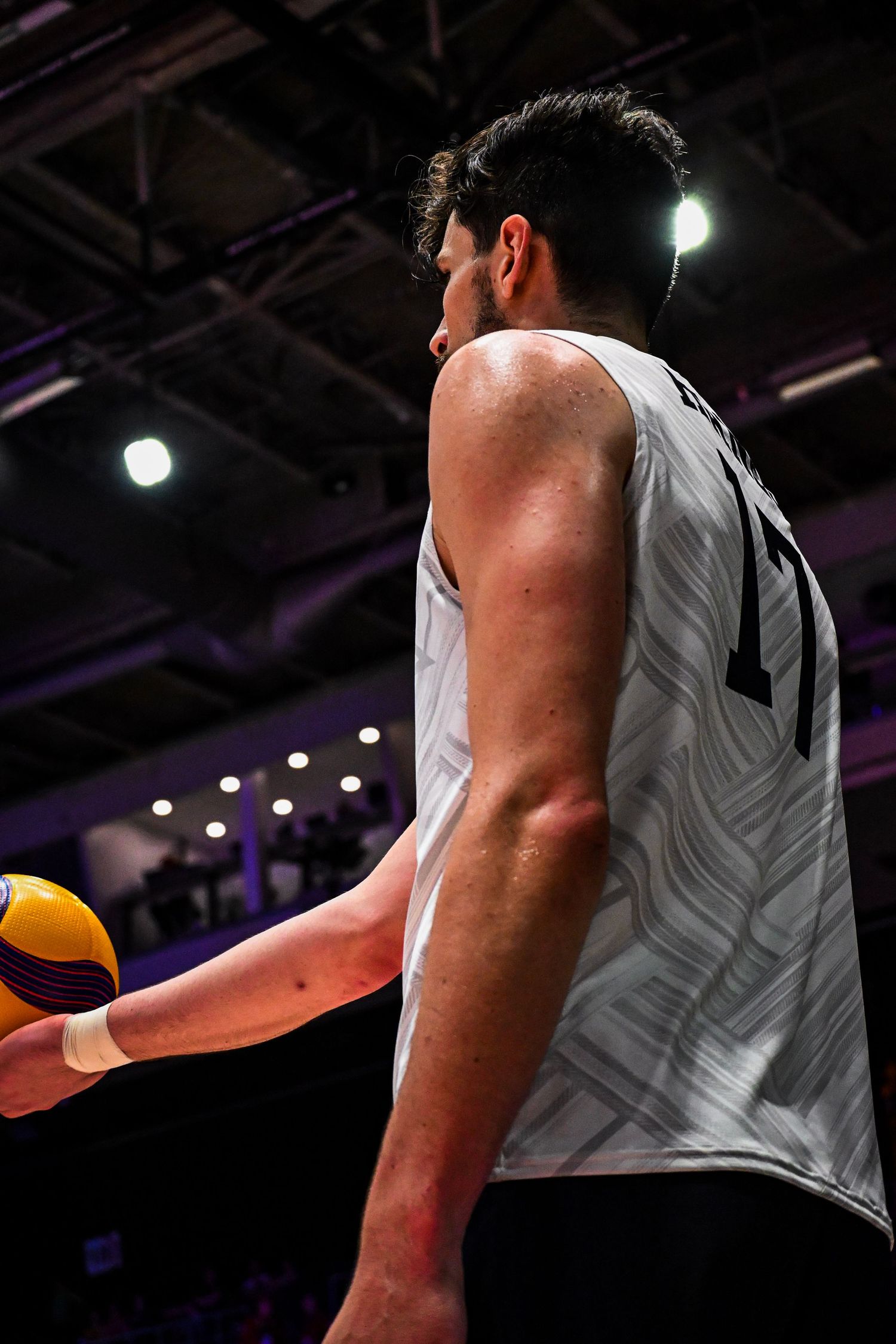 Profile view of a male basketball or volleyball player in a white jersey standing on the court.