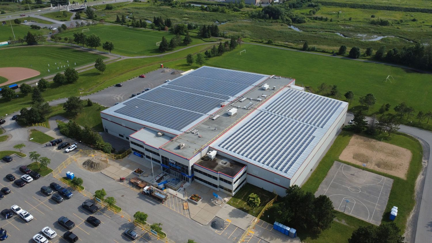 Aerial view of the Jim Durrell Recreation Centre in Ottawa, featuring large rooftop solar panel arrays, fields, and a parking lot.