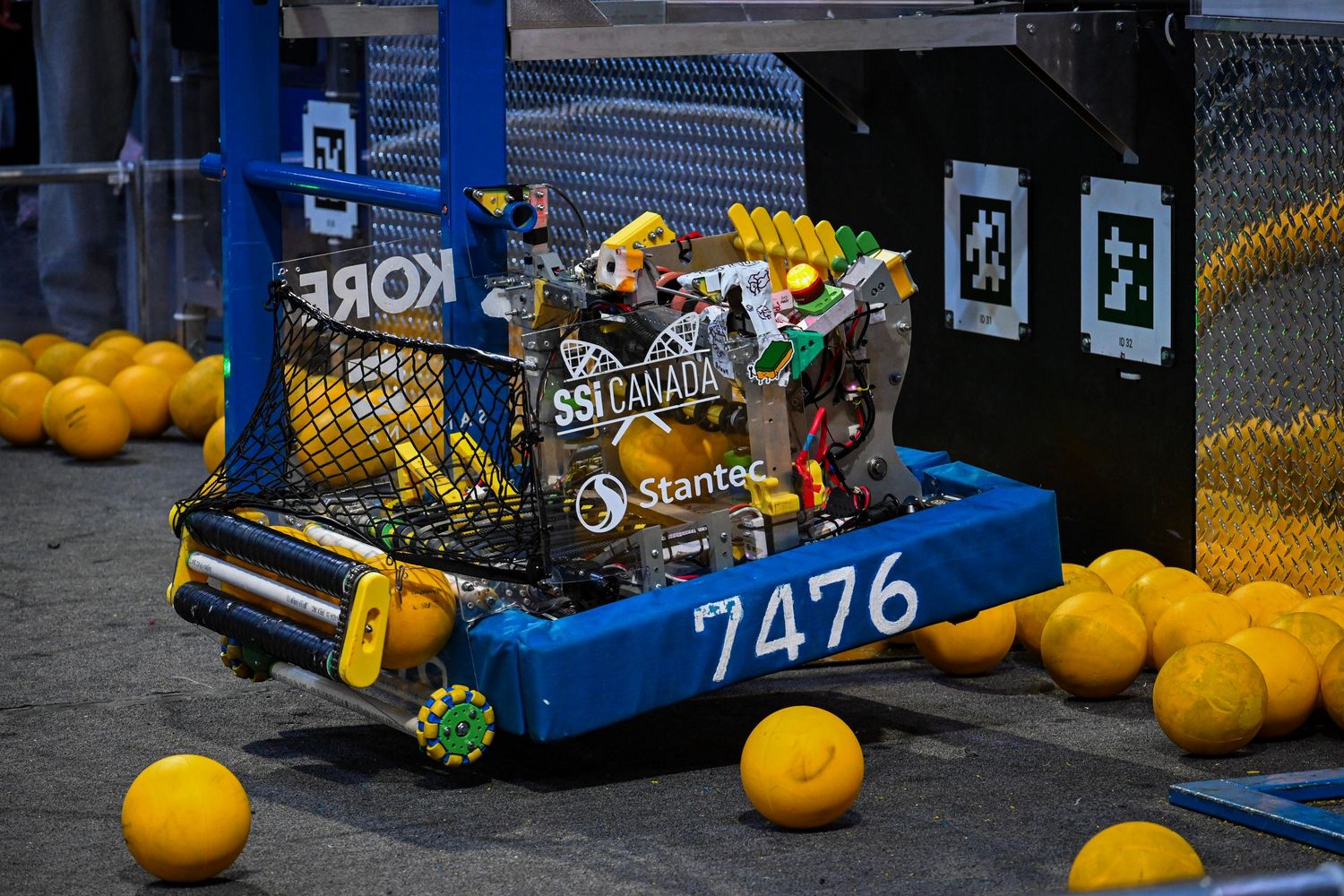 A close-up view of competition robot 7476 collecting yellow balls on an indoor tournament floor.