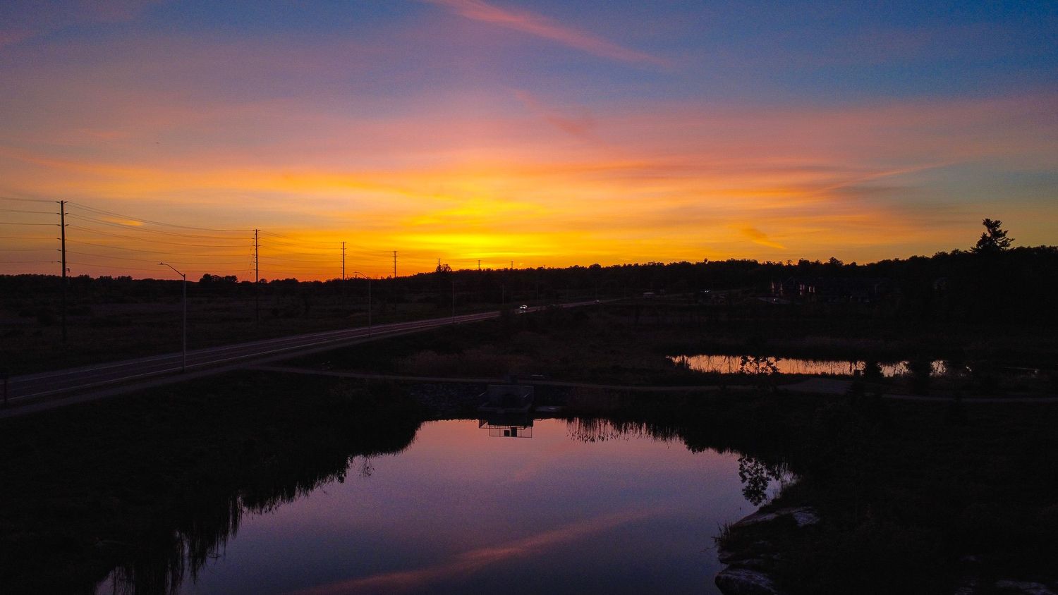 A wide drone aerial shot of a calm river reflecting a vibrant orange and purple sunset sky.