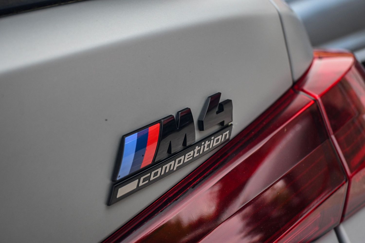 Close-up of a silver BMW M4 Competition car badge on the rear trunk.