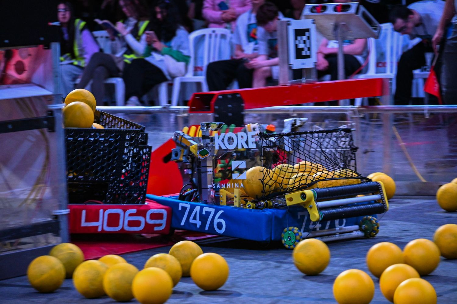 Competition robots numbered 4069 and 7476 facing each other on an indoor field covered in yellow balls.