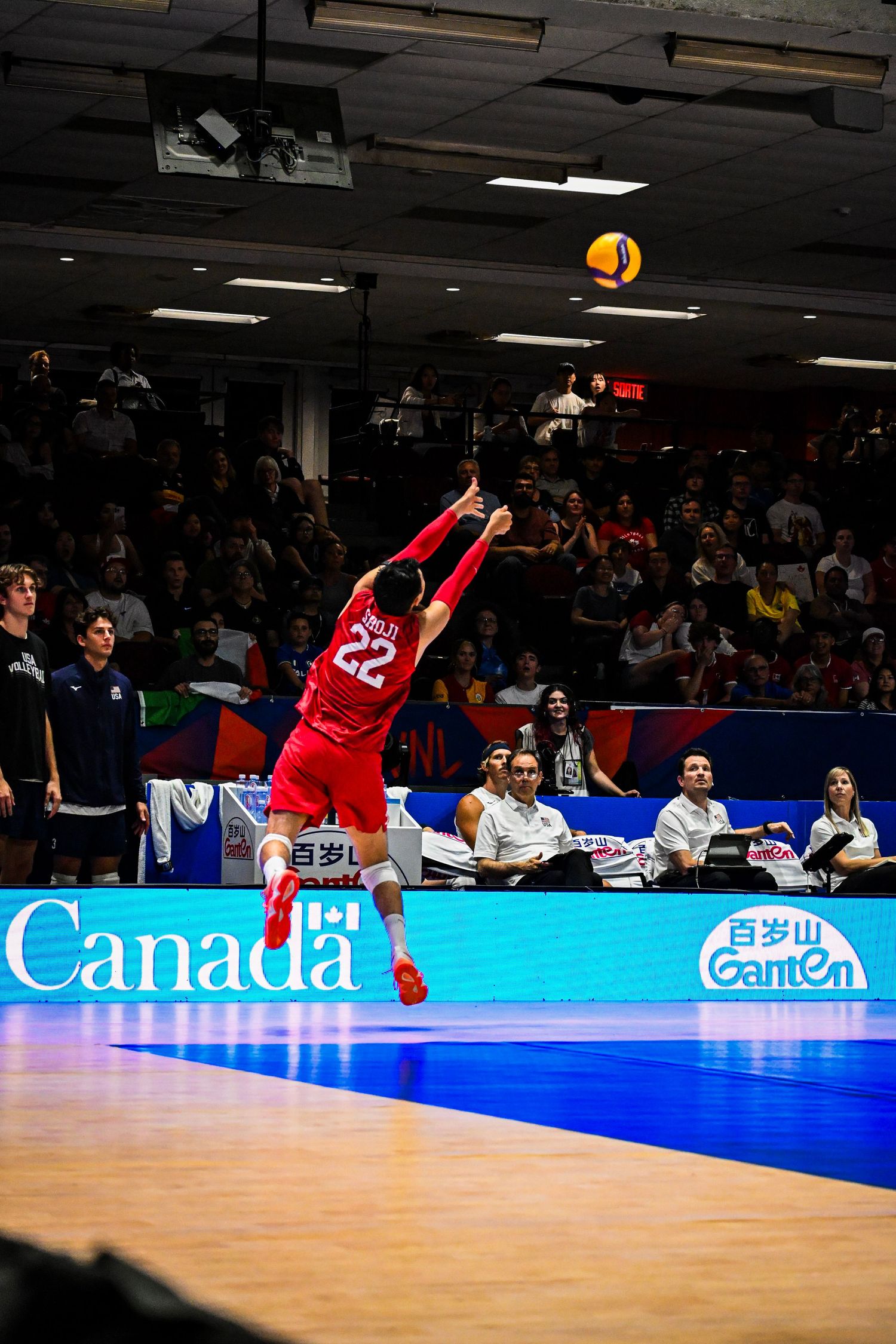 Volleyball libero in a red uniform dives horizontally to save and pass the ball during an indoor match.