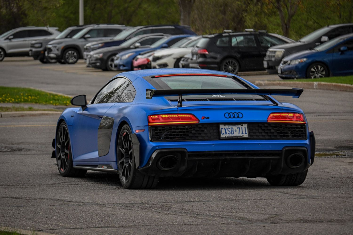 Rear three-quarter view of a bright blue Audi R8 sports car parked in a parking lot.