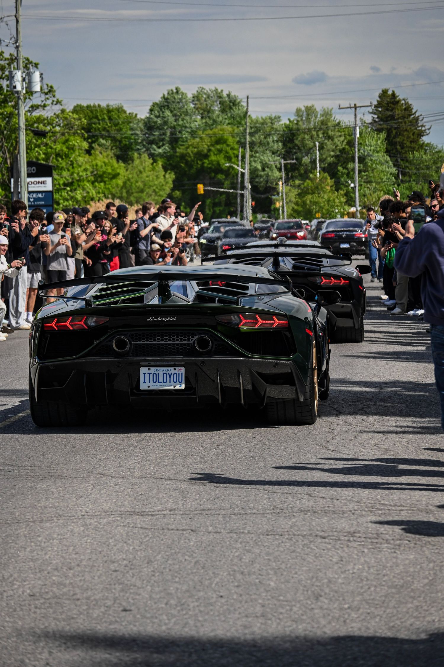 A Lamborghini driving down a paved street lined with a large crowd of spectators.