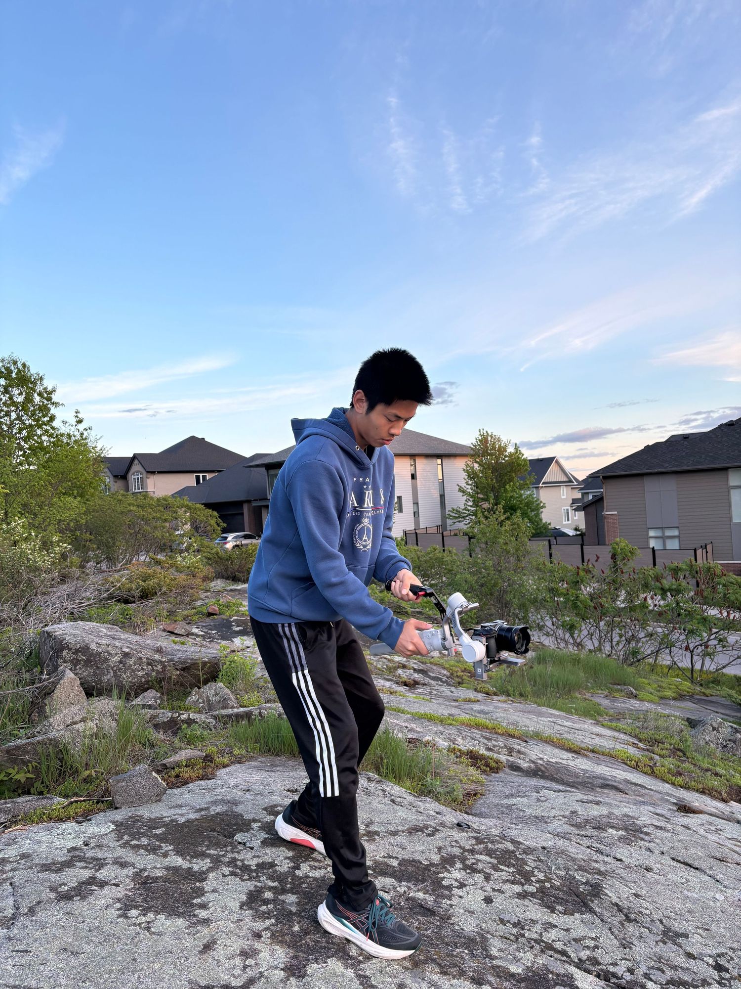 Full-body shot of a person operating a camera gimbal on a rocky outdoor landscape under a blue sky.