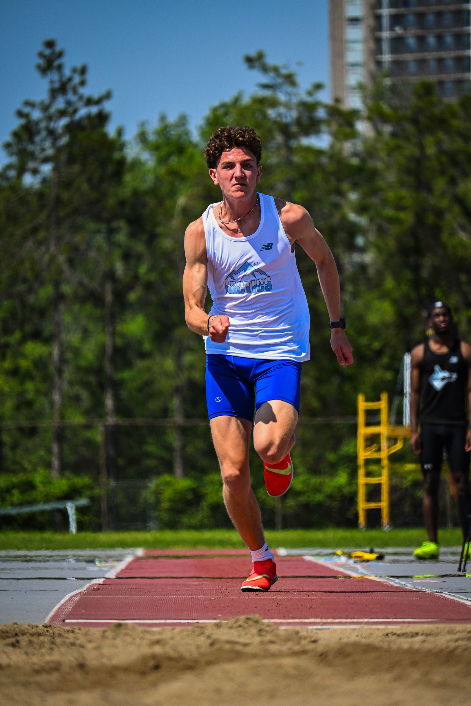 An athlete in a white singlet sprinting down a track toward the camera.
