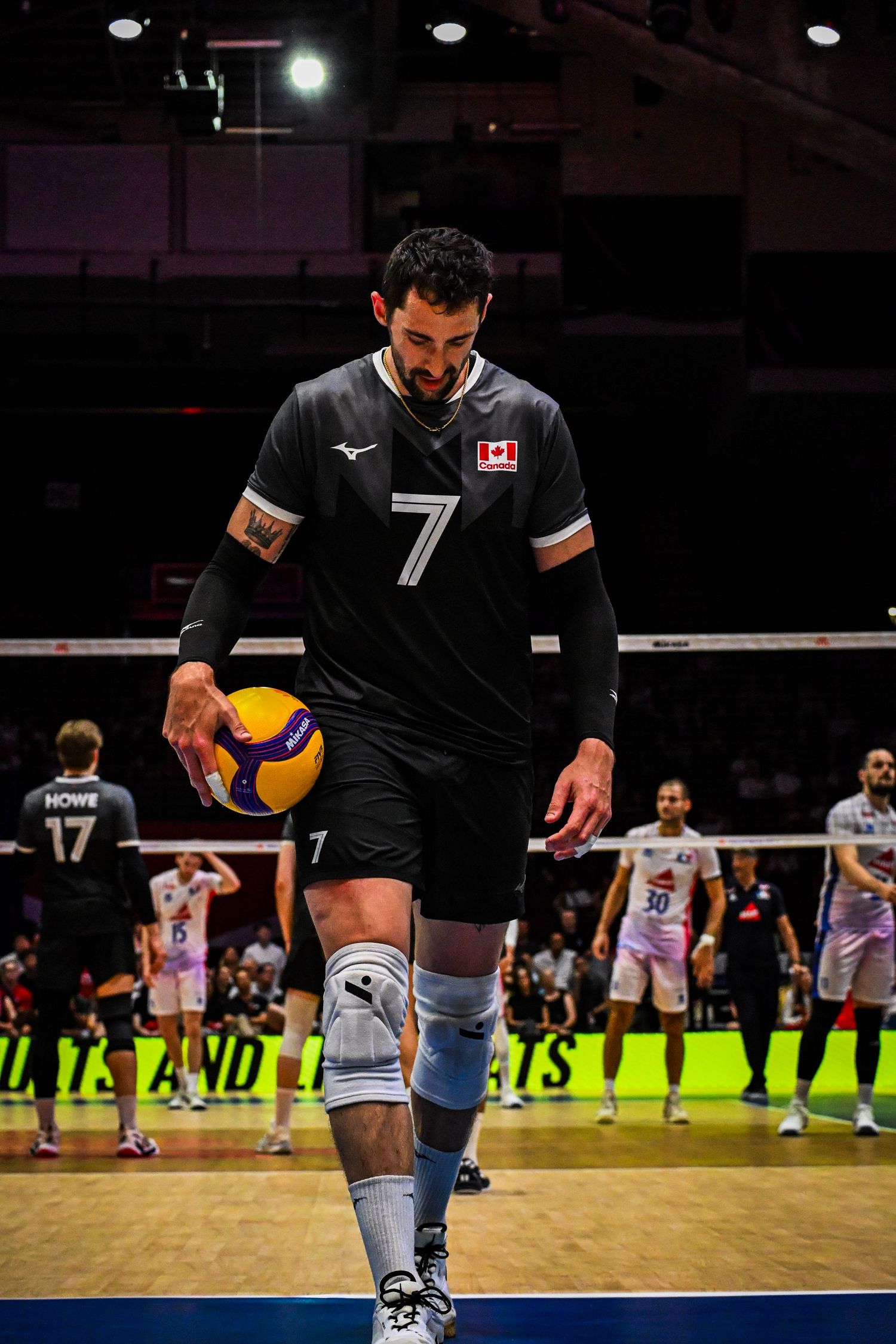 Volleyball player wearing black jersey number 7 stands on the court holding a volleyball.