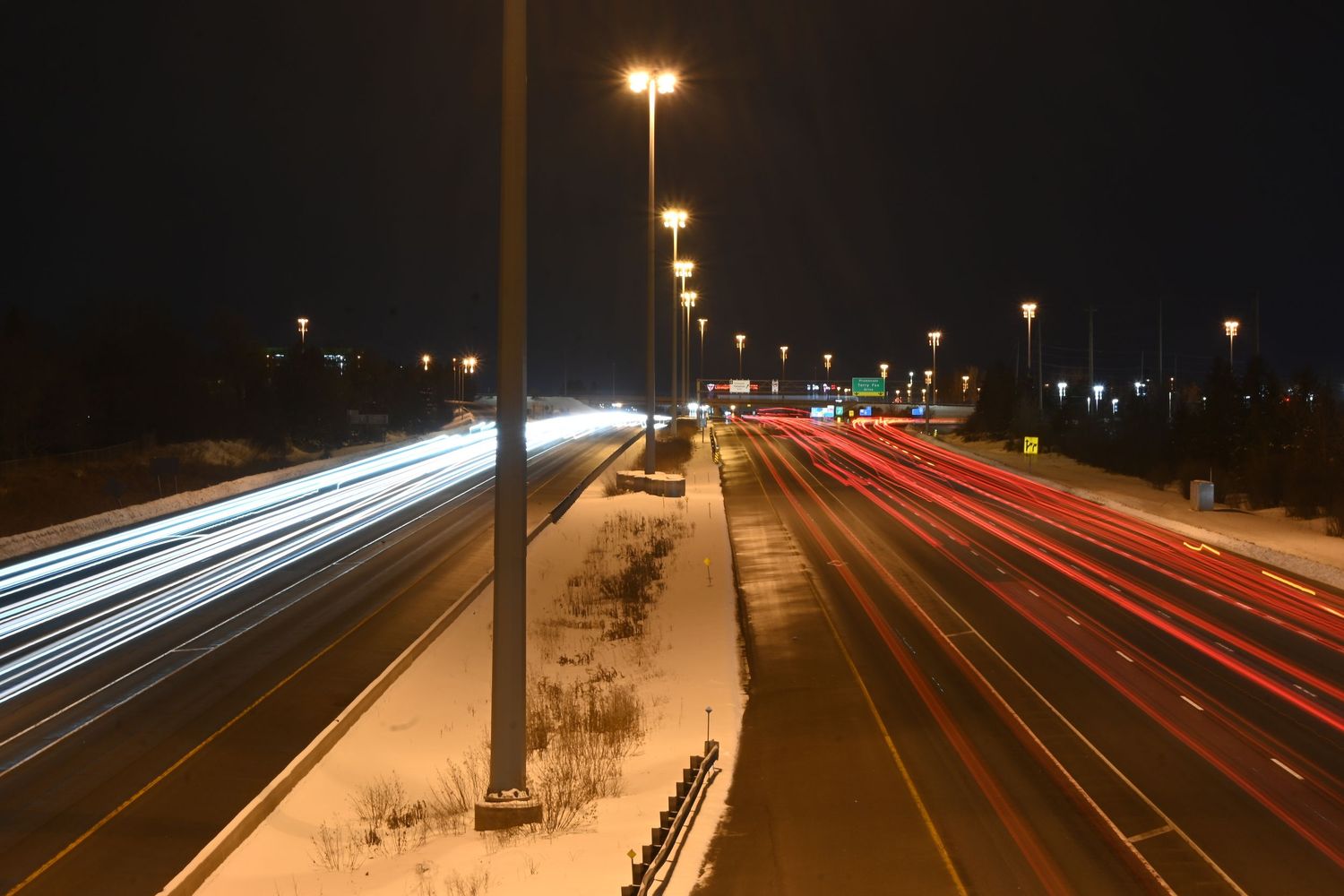 A long-exposure night shot of highway traffic showing streaks of white and red light trails.