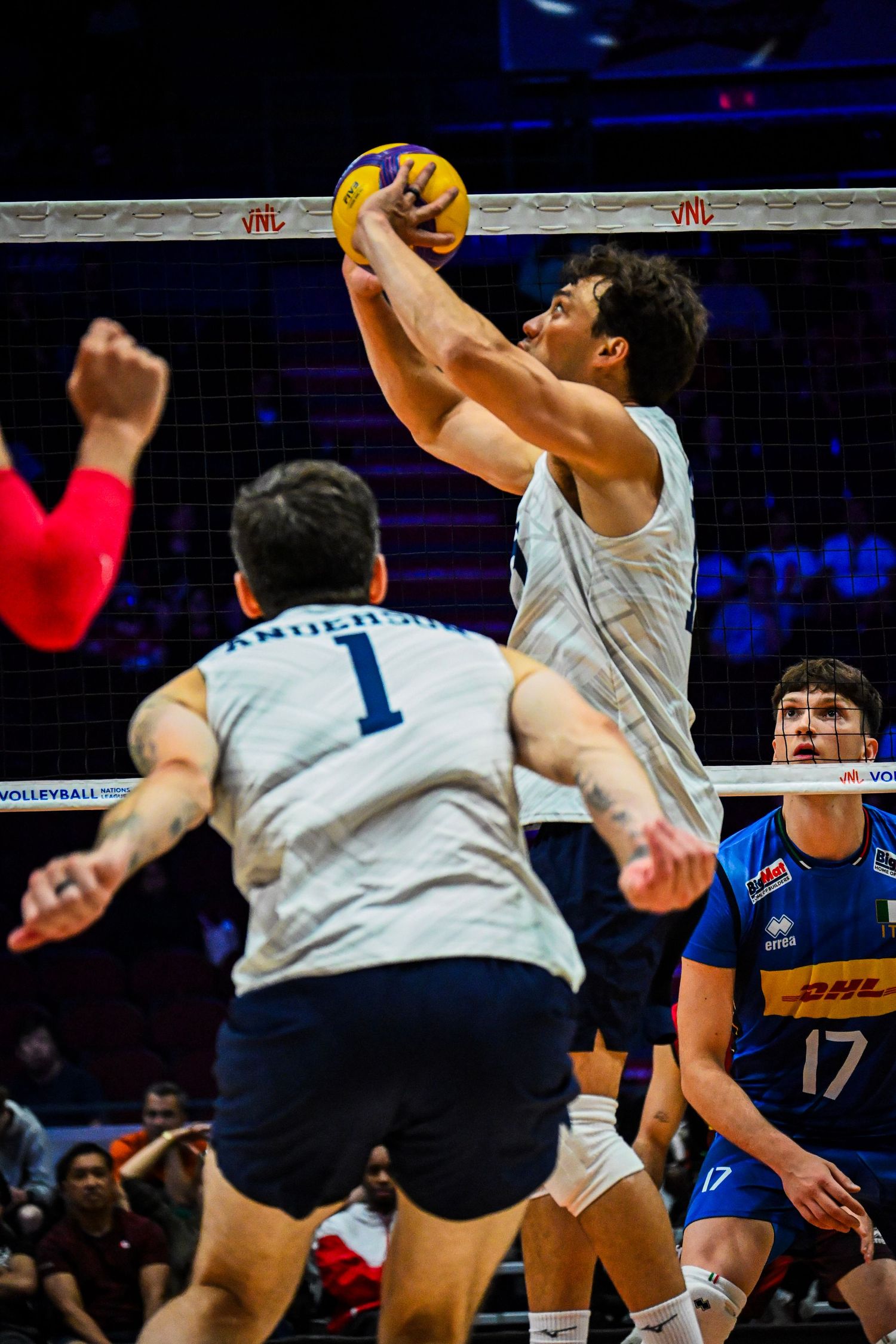 Volleyball setter leaps to set the ball mid-air for his teammates during an indoor match.