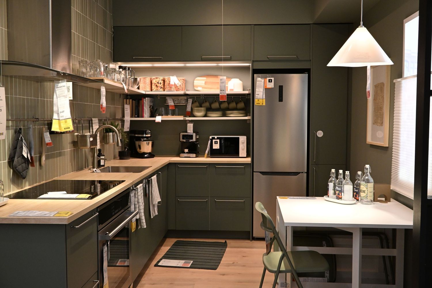 This is a modern, modular showroom kitchen from IKEA featuring dark matte olive green cabinets paired with a light wood-look countertop.