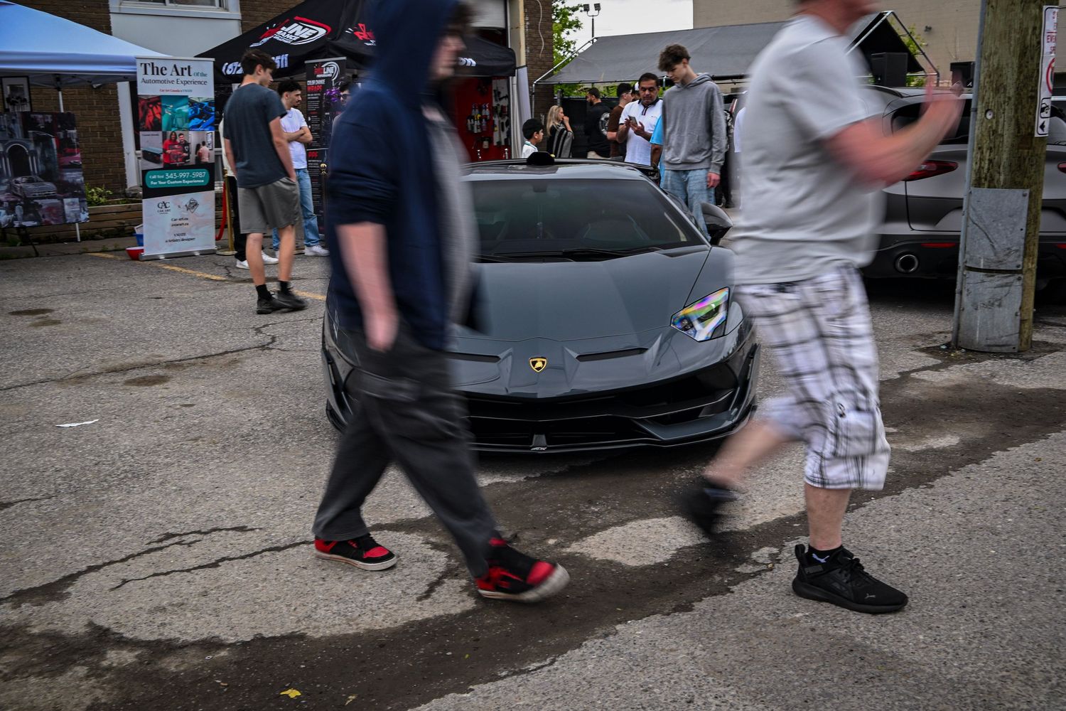 People walking past a matte gray Lamborghini parked at an outdoor car meet.