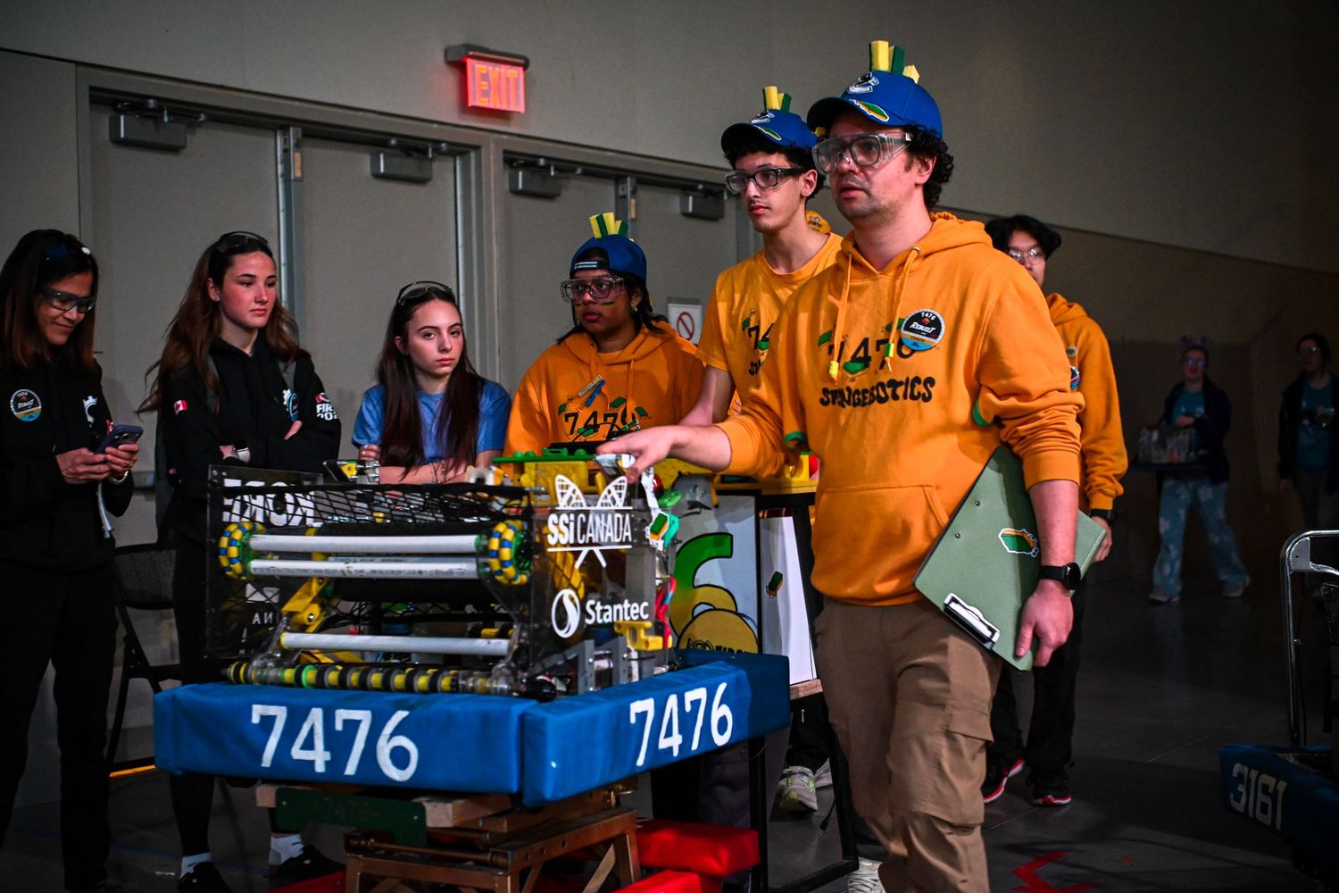 Robotics team members gathered around competition robot 7476 in a staging area.