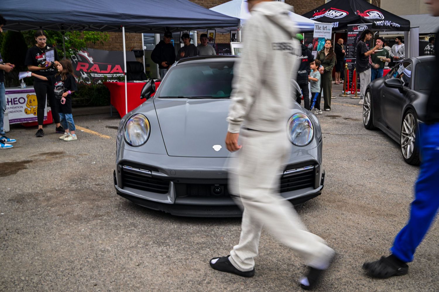 Front view of a gray Porsche sports car parked at an outdoor car event with people walking past in the foreground.