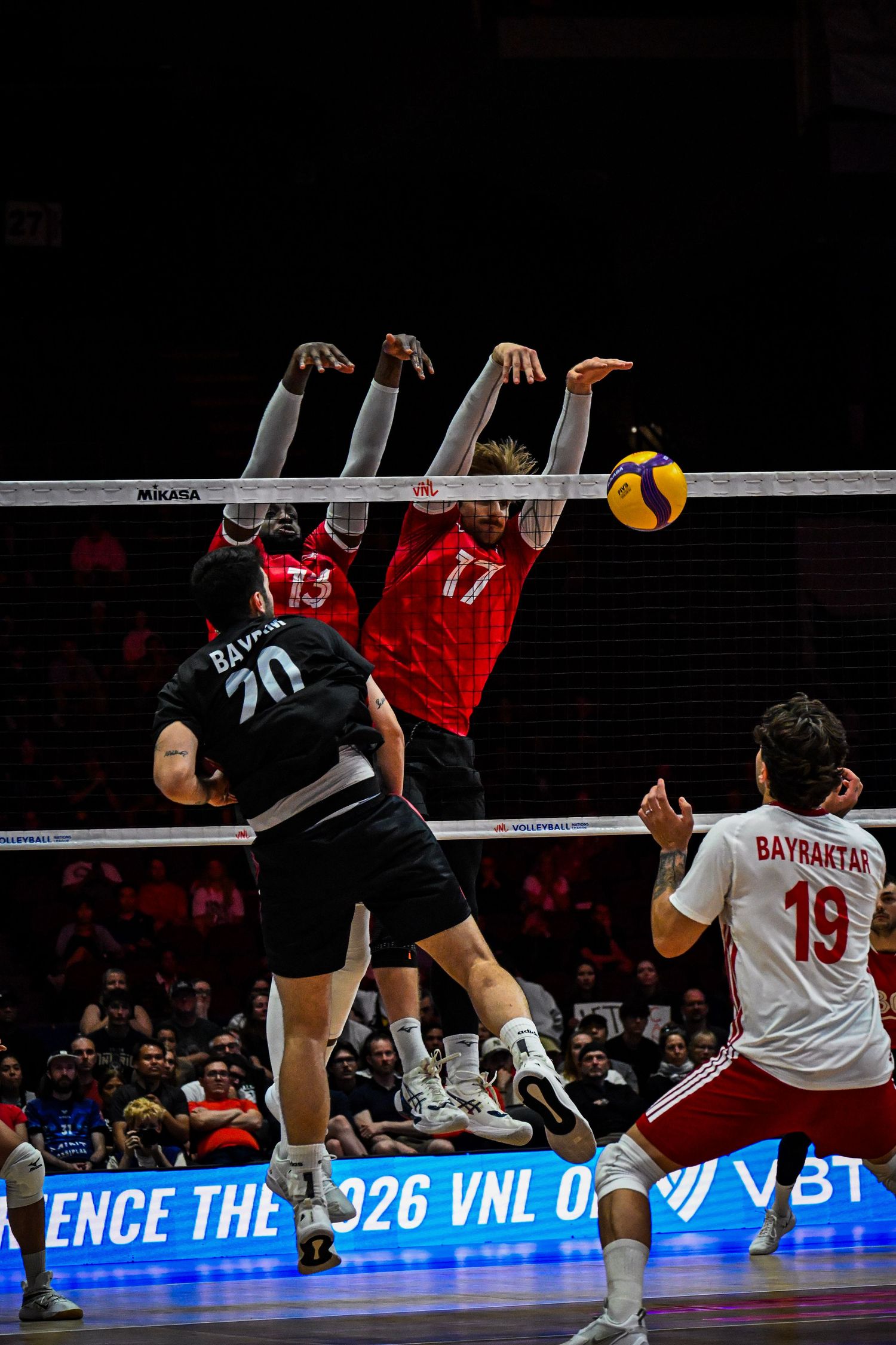 A volleyball player leaping high at the net to spike the ball during an indoor match.