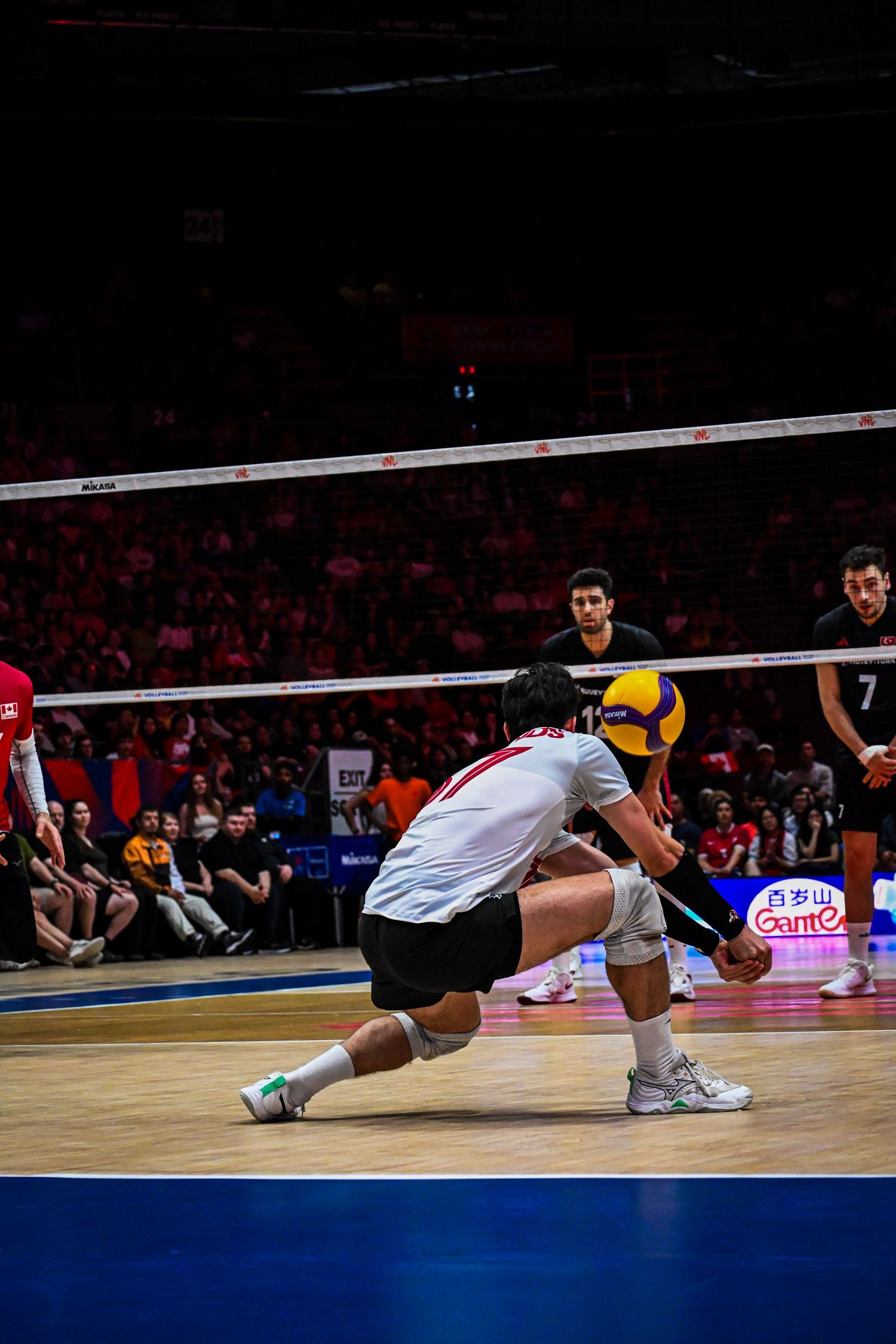 Volleyball player in a white jersey crouches low on the court ready to pass the ball.