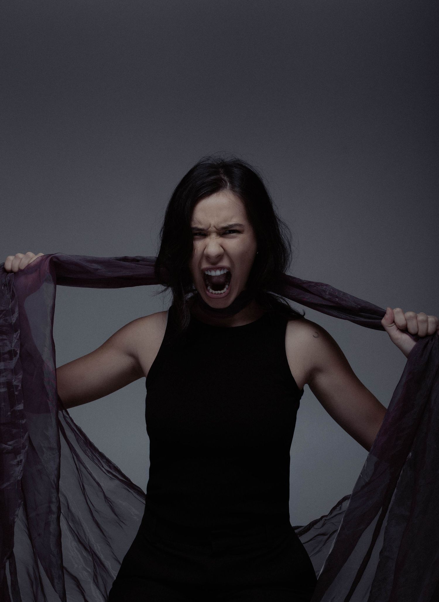 A woman in black screams while tearing apart a dark purple fabric in a dramatic studio shot.