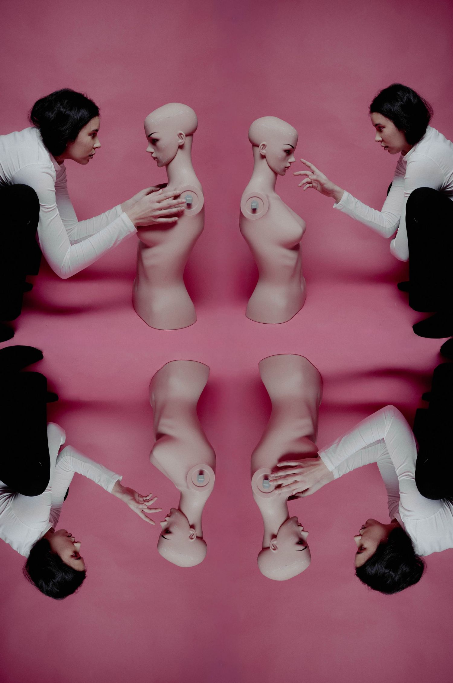 Surreal mirrored image of woman in white interacting with nude mannequin torso on pink background.