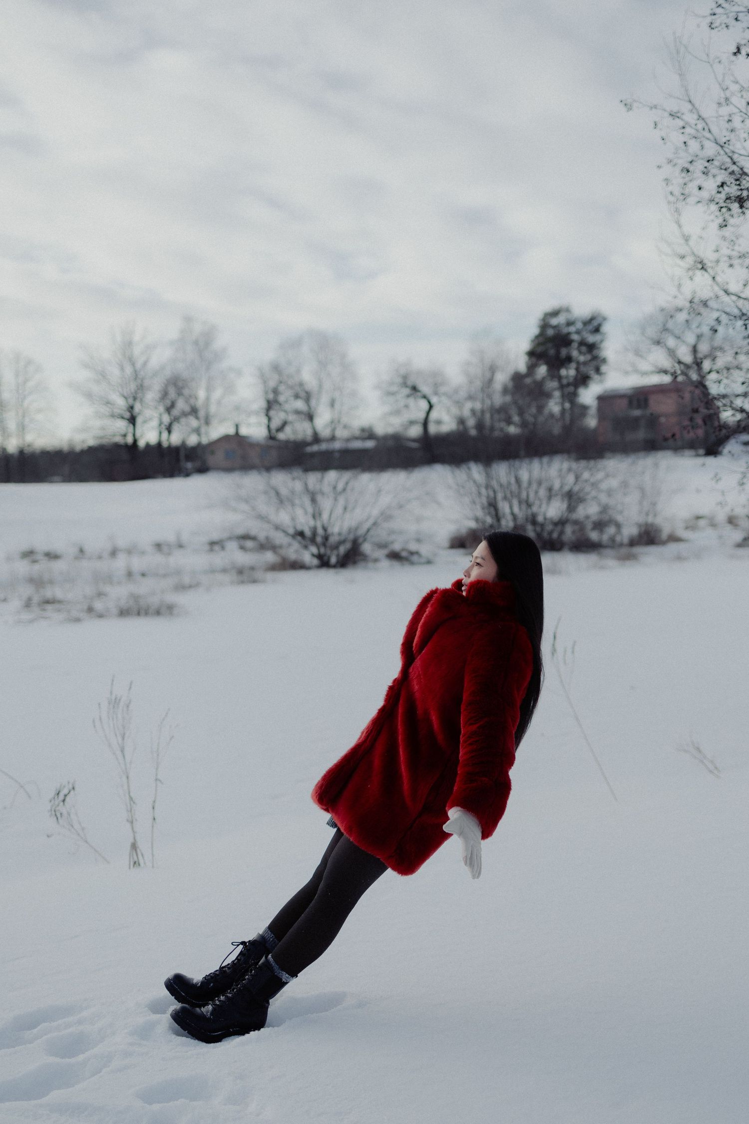 Woman in red fur coat leaning back in snowy winter landscape.