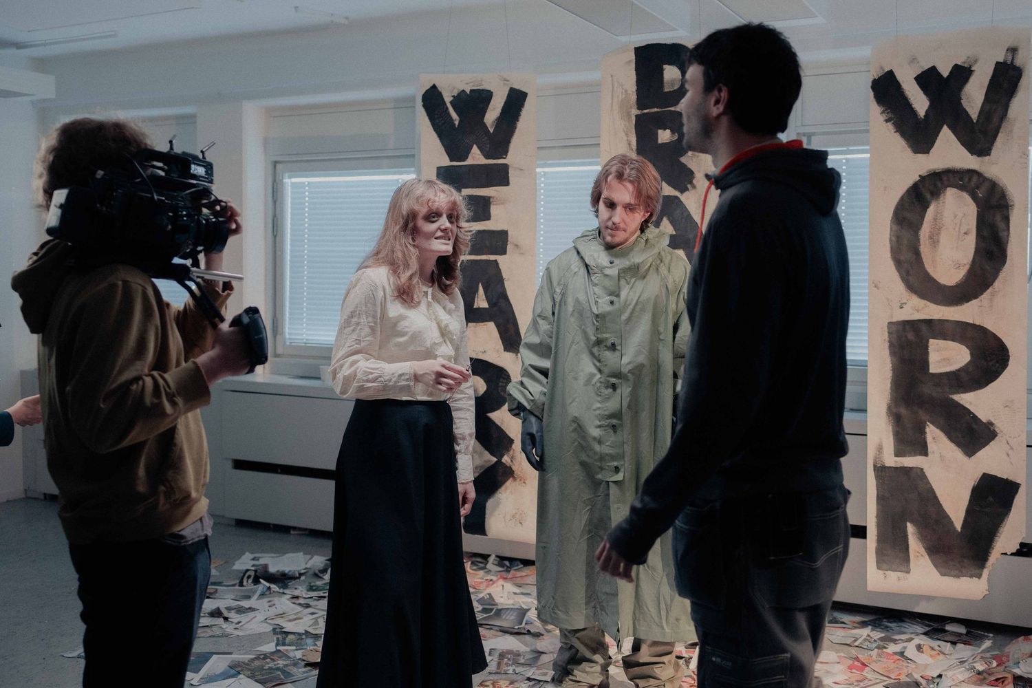 Film crew interviewing people in front of large text art installations spelling WEAK and WORN.