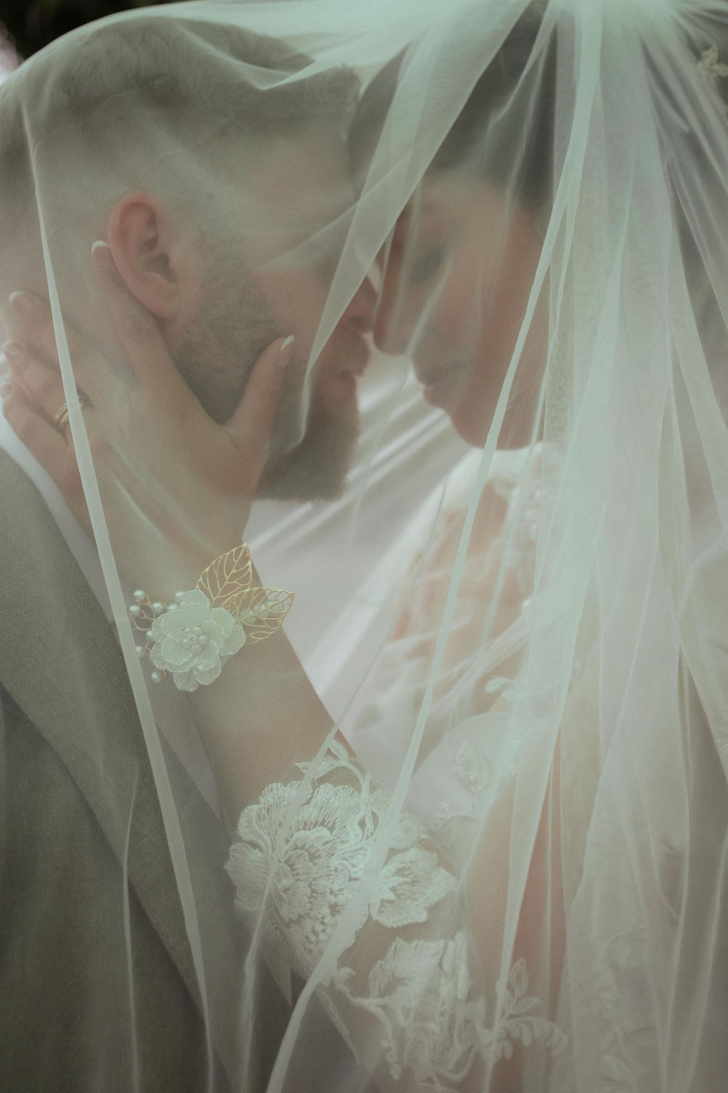 Intimate wedding couple almost kissing under a flowing white bridal veil.