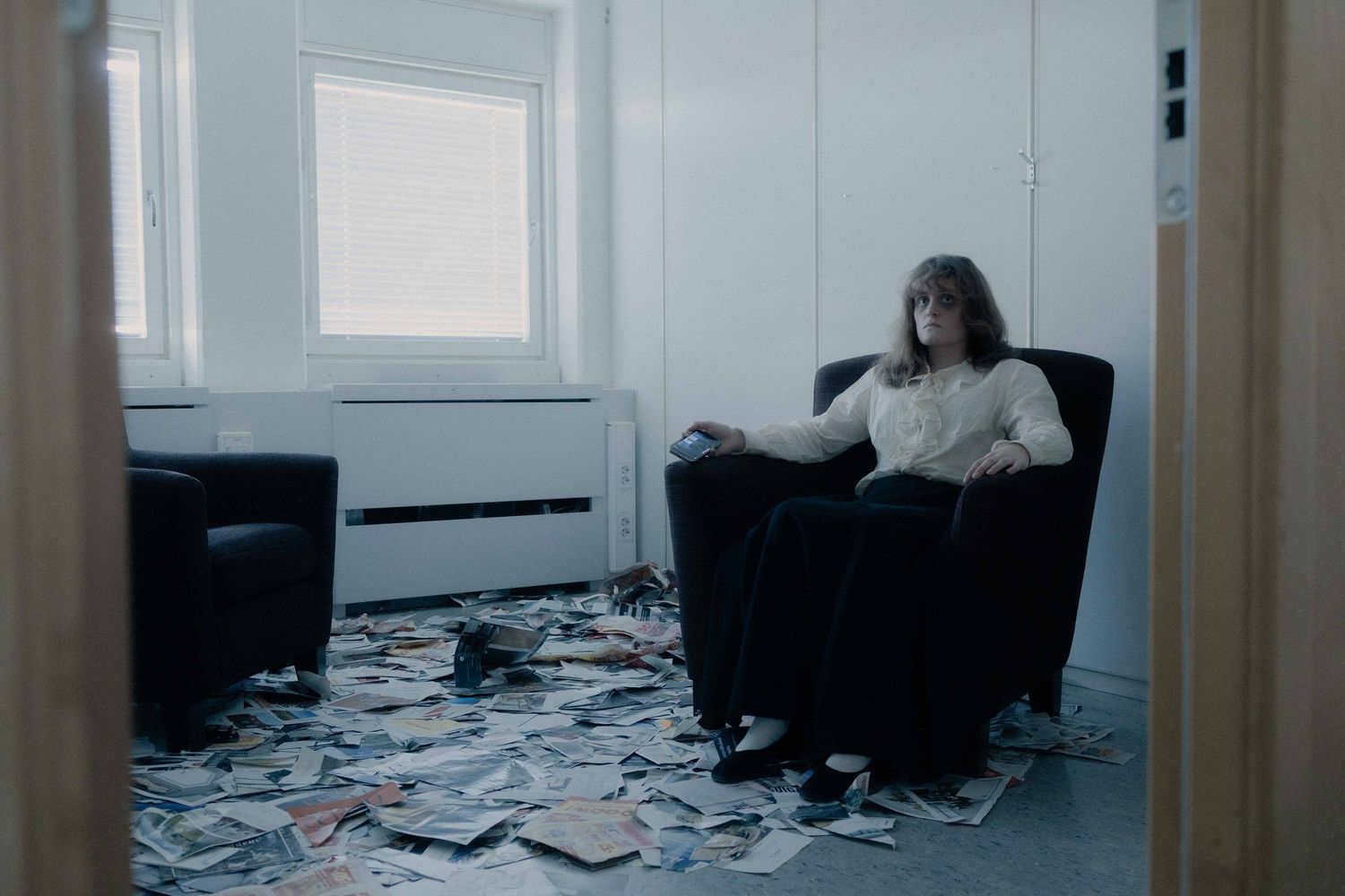 Person sitting in black armchair surrounded by scattered papers on a bright office floor.