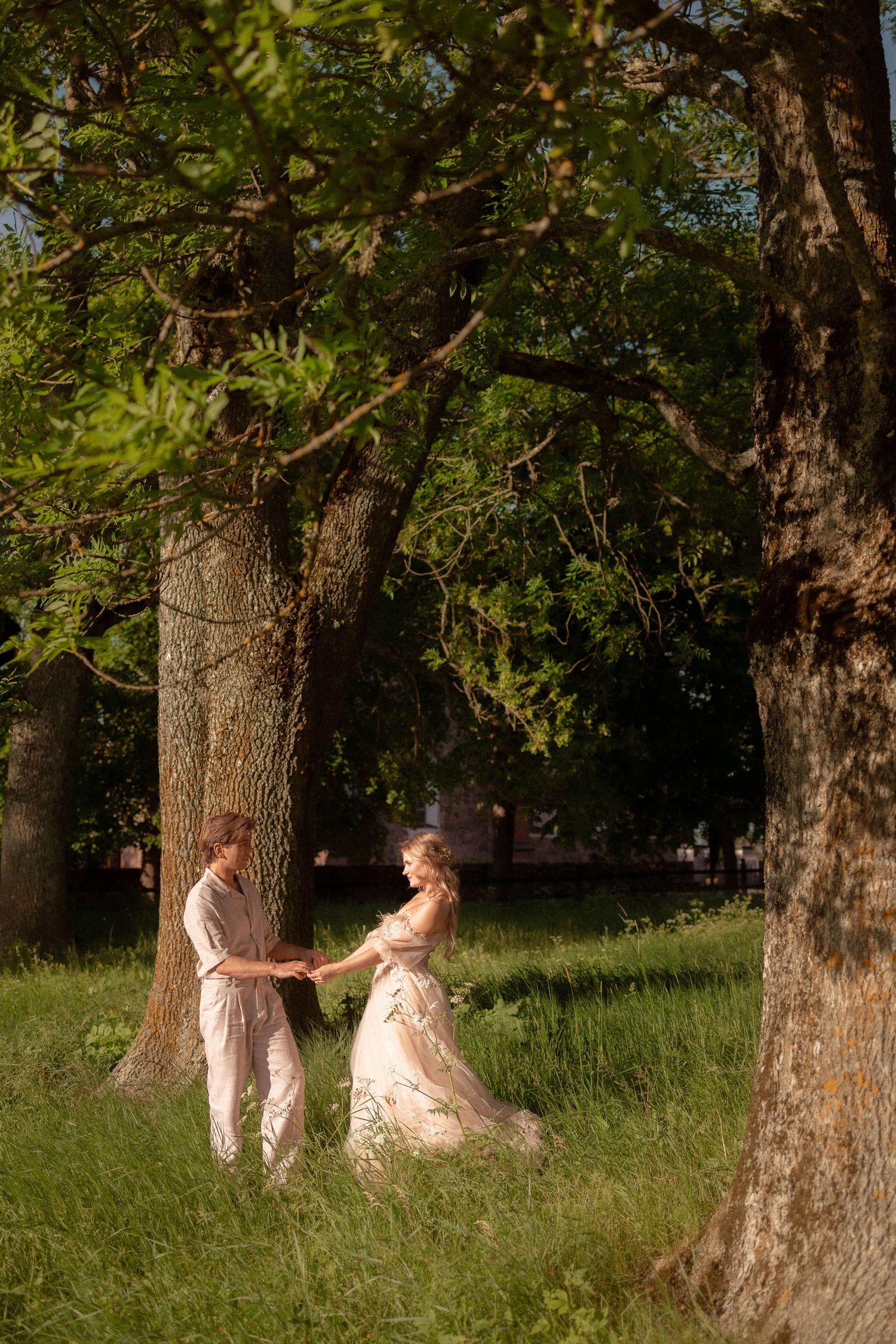 Bride and groom holding hands among tall trees in a sunlit forest clearing.
