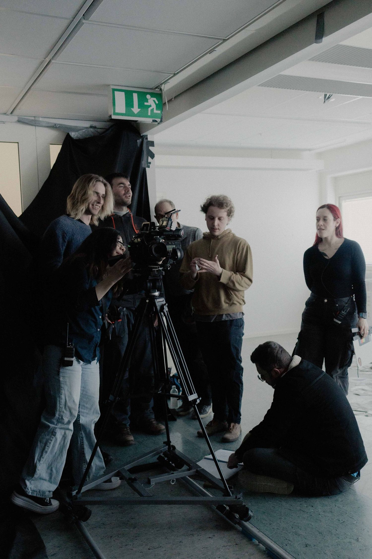 Film crew gathered around a camera on a dolly track in a bright studio corridor.