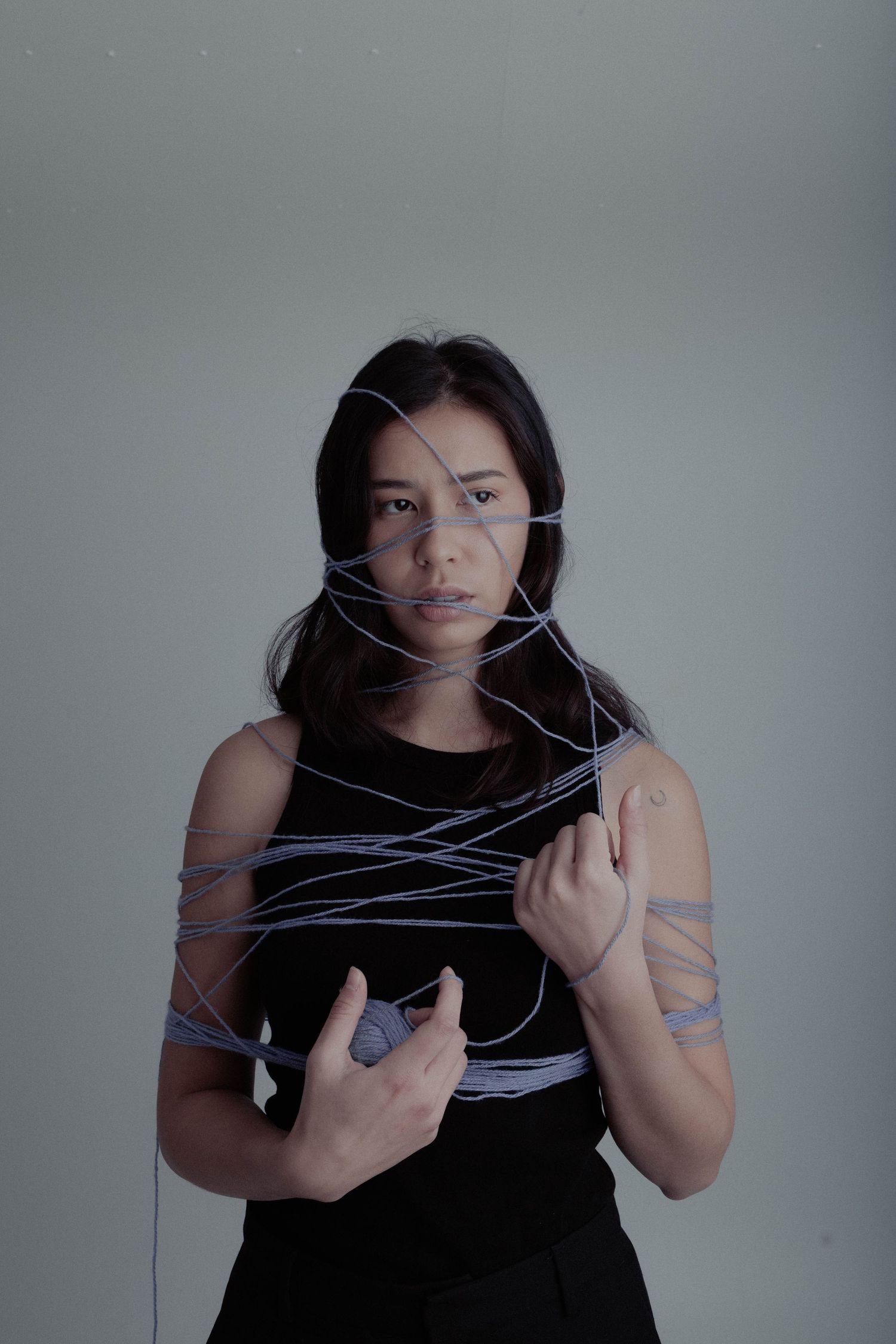 Woman wrapped in blue yarn holding a ball of thread, artistic conceptual portrait photography.