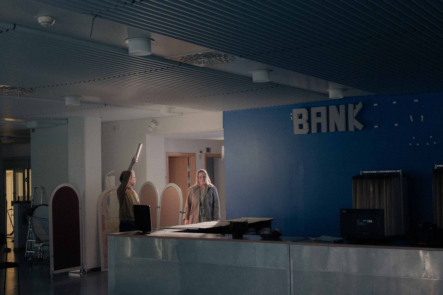 Two people standing at a bank reception desk in a dimly lit blue-themed interior.