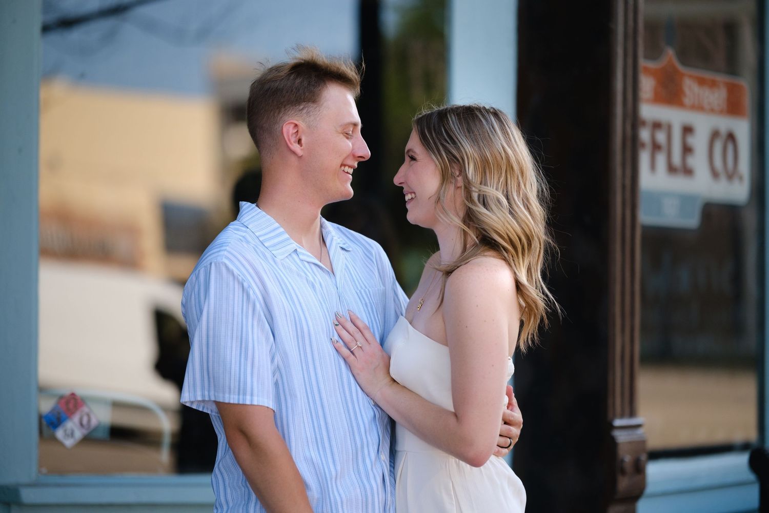 Happy couple sharing a romantic moment outside a waffle shop, woman in white dress touching mans chest.