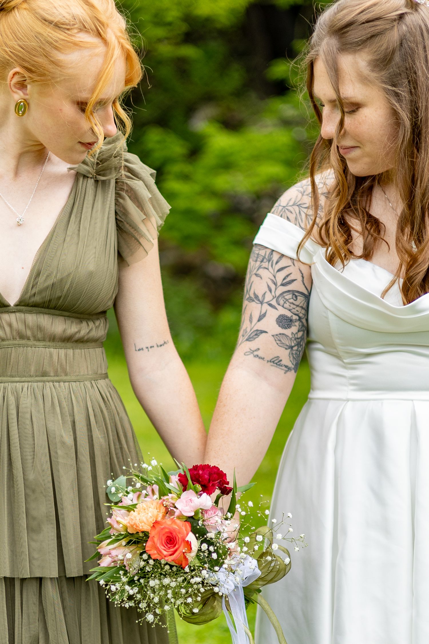 Two brides holding a colorful bouquet of roses in an outdoor garden wedding ceremony.