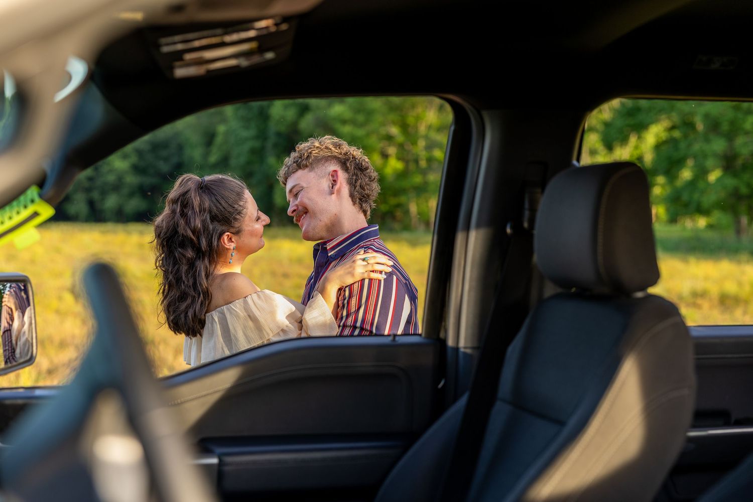 A couple sharing an intimate moment viewed through a truck window with a golden sunset in the background.