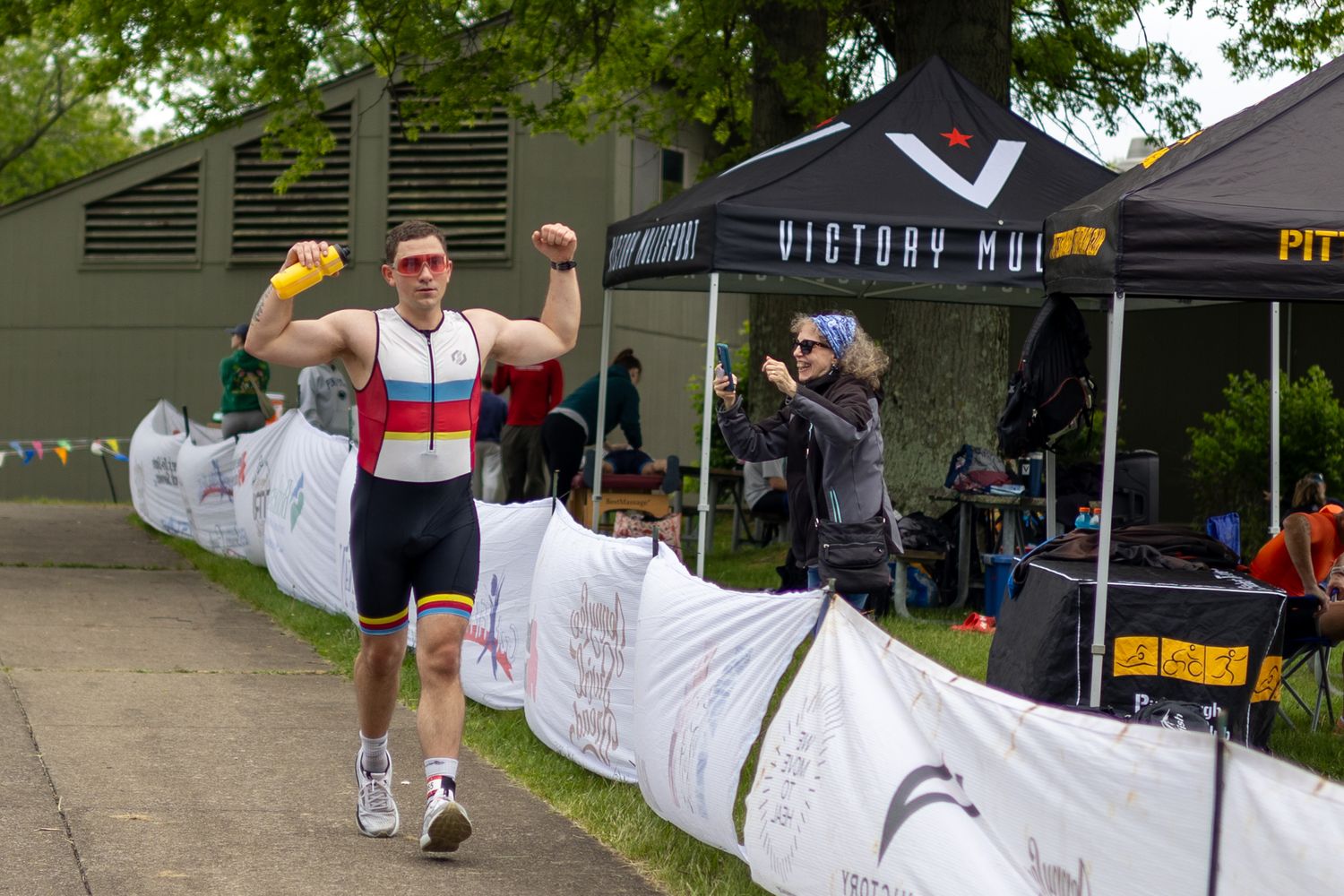 Triathlete flexing arms in celebration crossing finish line at Victory Mud race event outdoors.