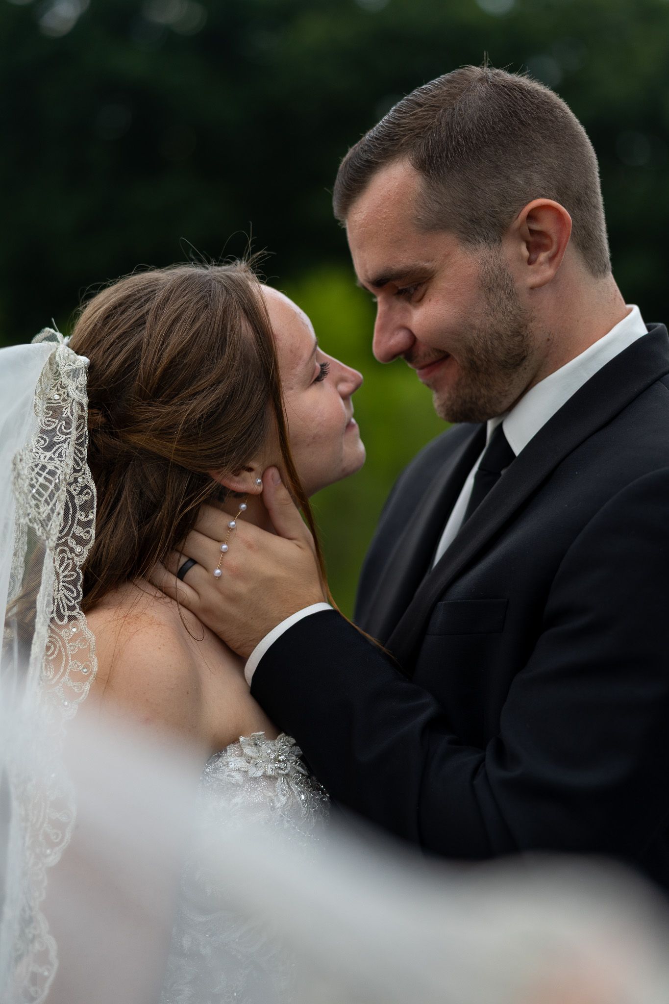 Groom tenderly holding brides face as they share intimate moment outdoors on their wedding day.