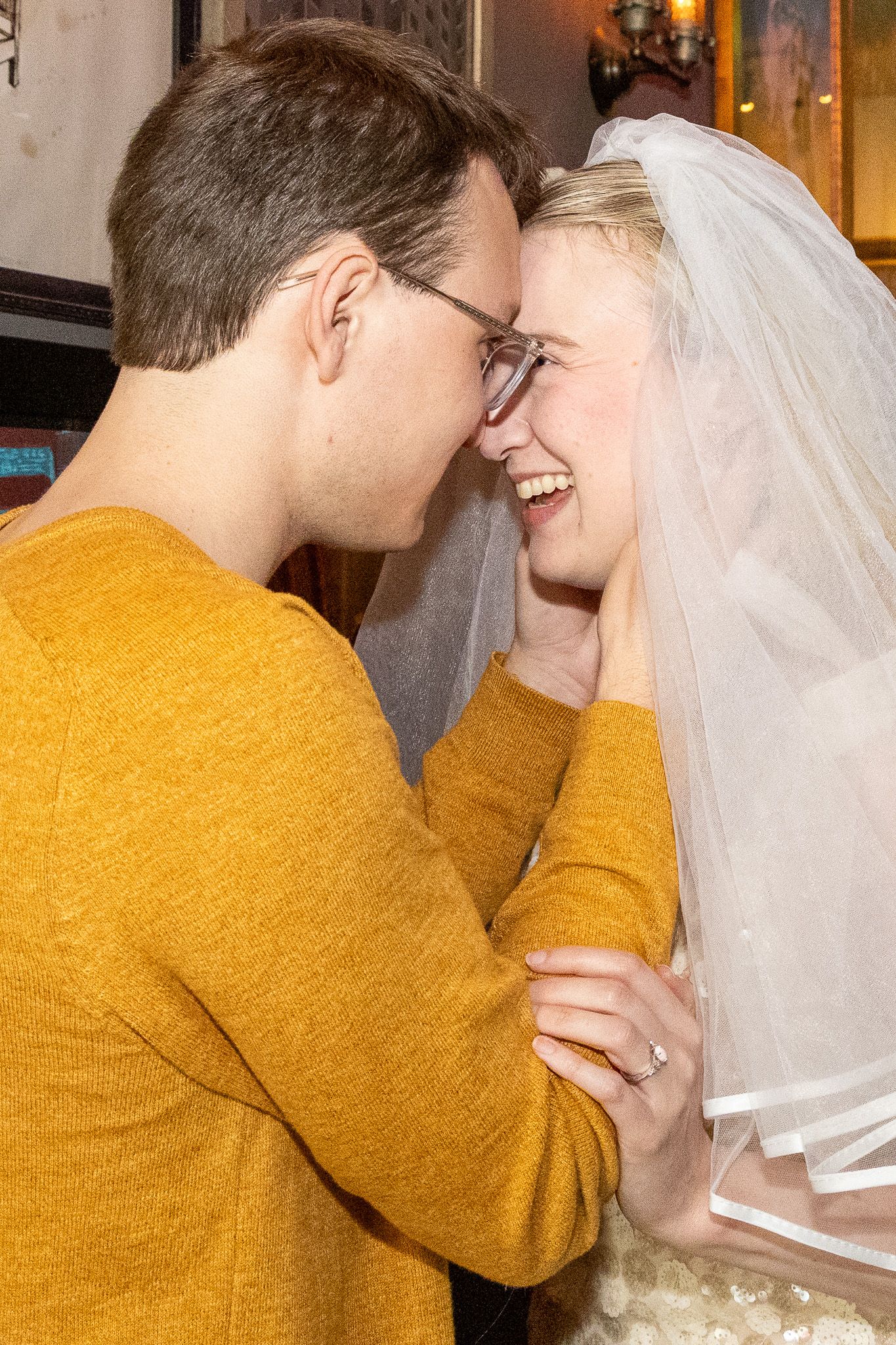 Happy couple sharing intimate moment, bride in veil laughing with man in mustard yellow sweater.