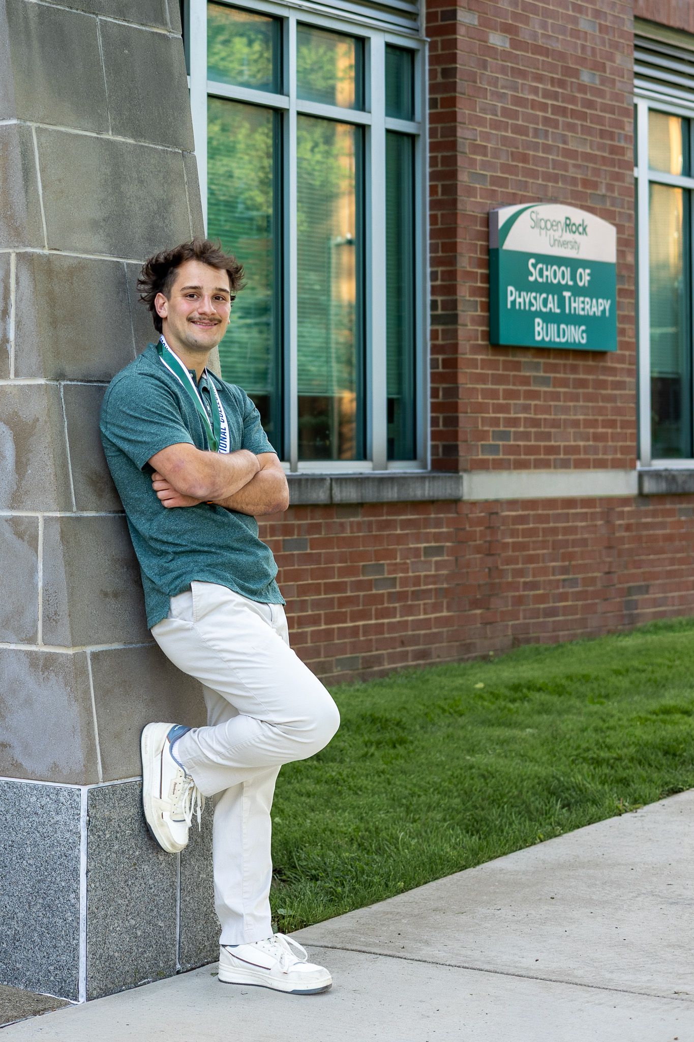 Male student leans against wall outside Slippery Rock University School of Physical Therapy Building.